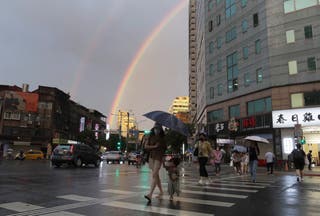 People walk in the rain with a backdrop of the rainbow in the sky as Typhoon Krathon approaches to Taiwan in Taipei