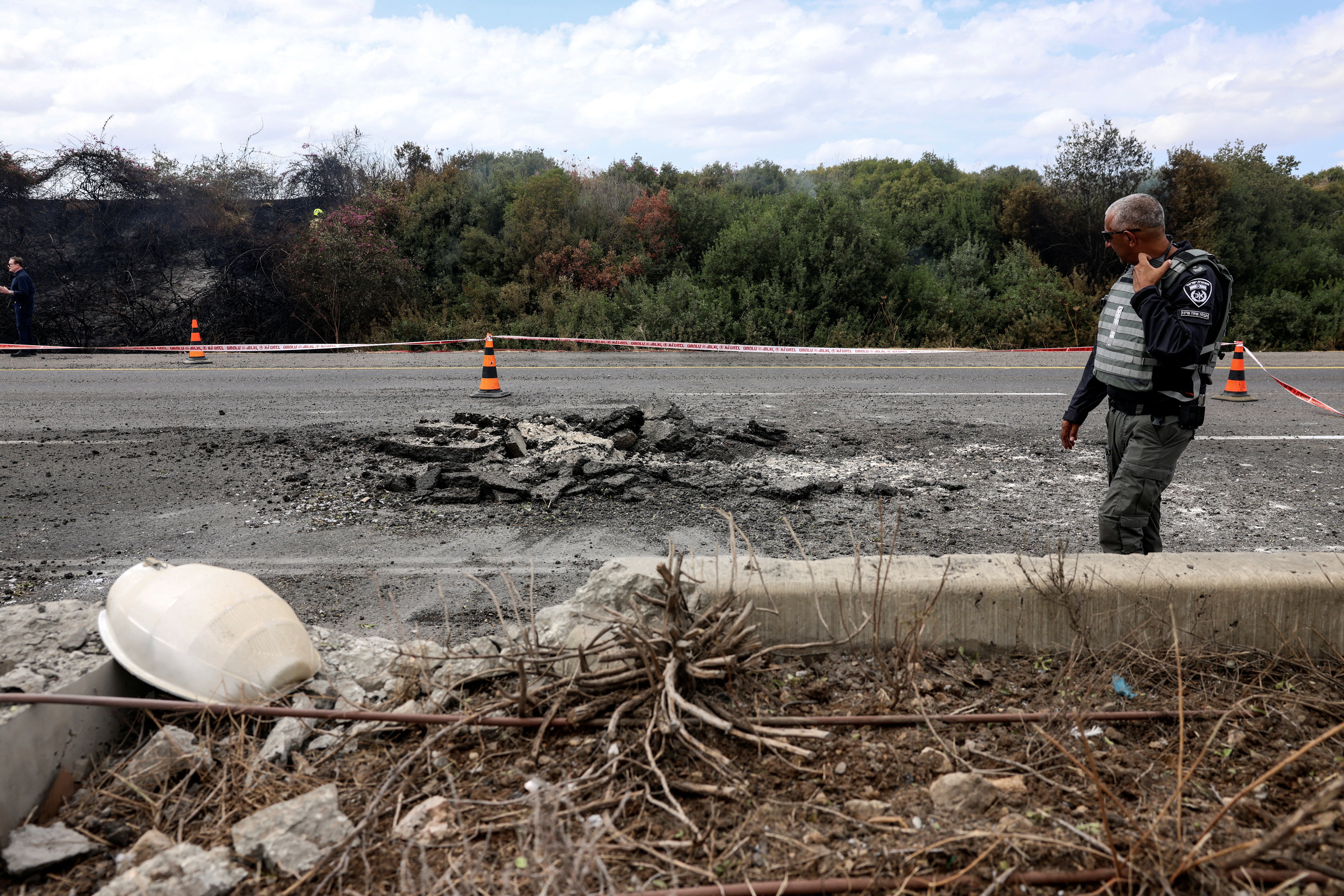 An Israeli police officer looks at damage to a highway caused by a rocket, fired from Lebanon into Israel near Kfar Qasim, Israel