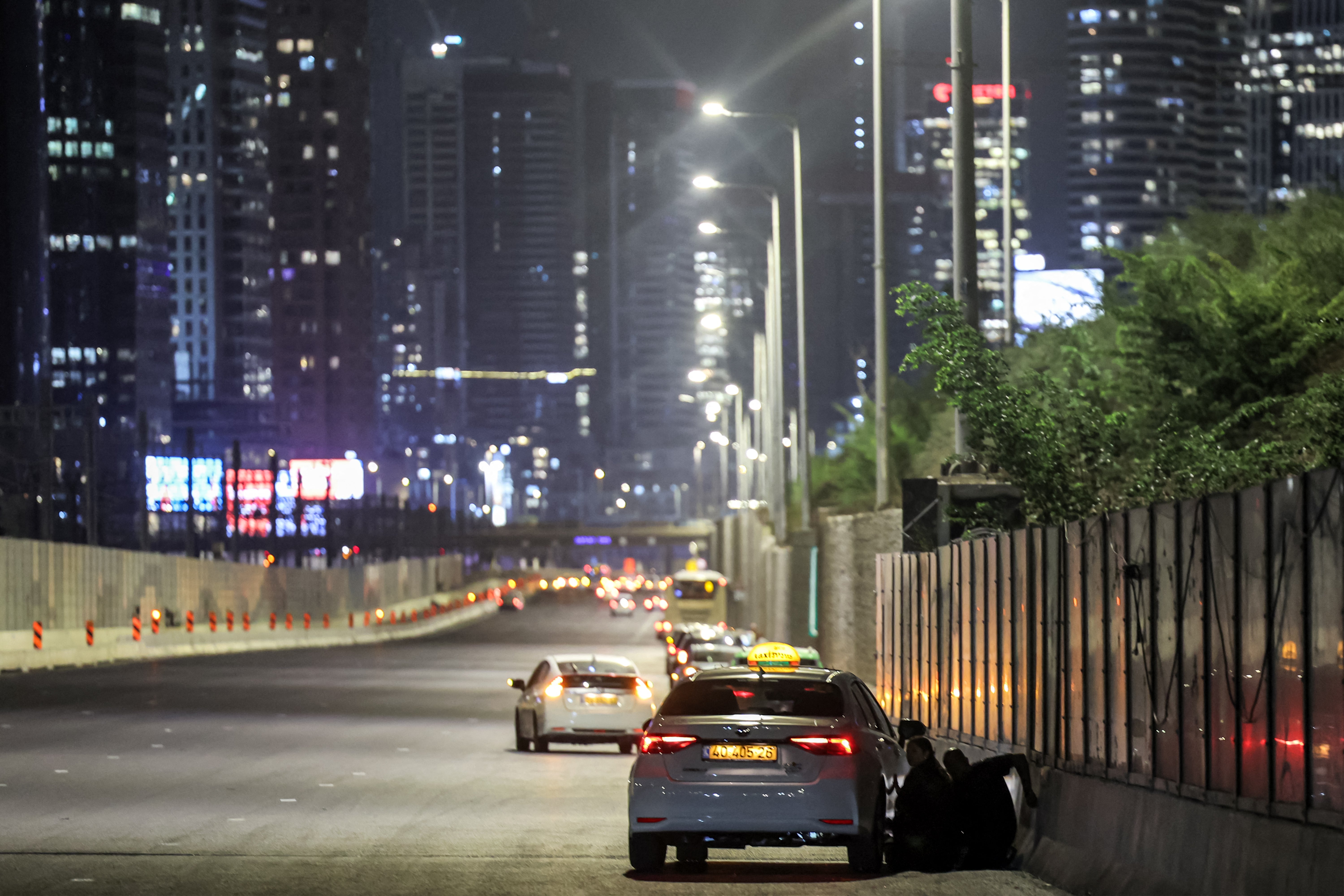 People take cover behind a vehicle parked along the side of a highway in Tel Aviv