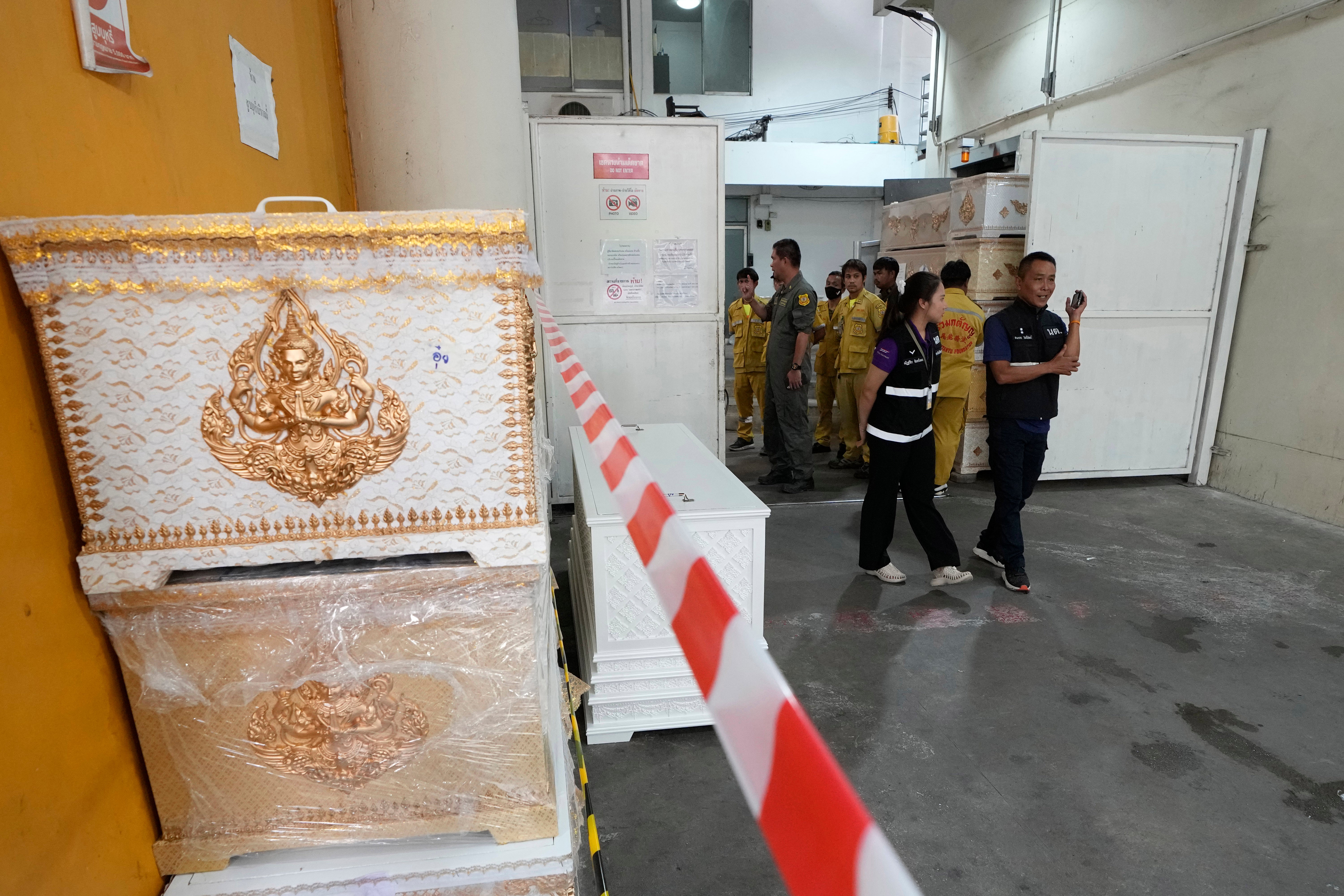 Forensic officers stand beside empty coffins at a forensic police hospital in Bangkok, Thailand