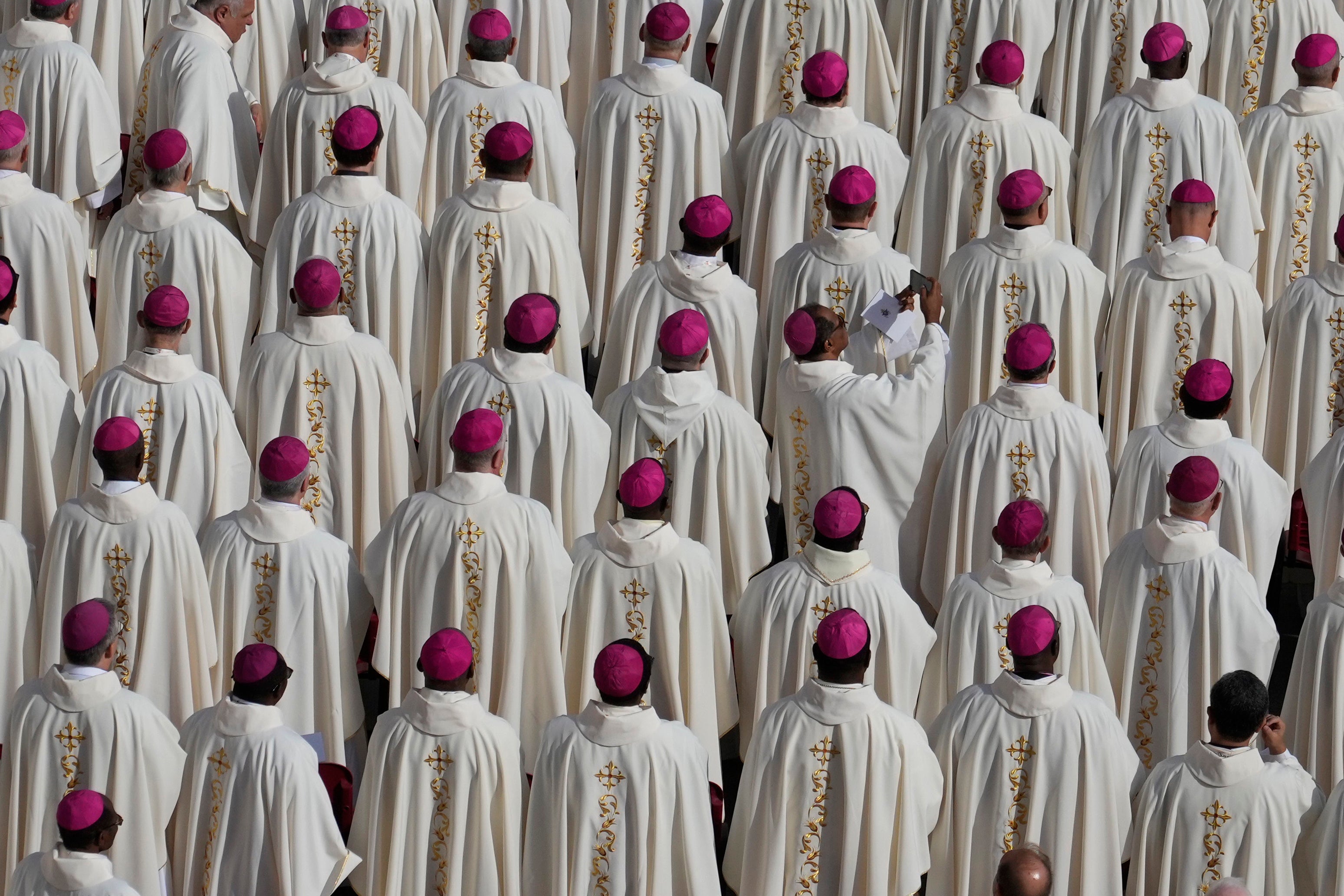 A bishop uses a smartphone as Pope Francis presides over a mass in St. Peter’s Square,