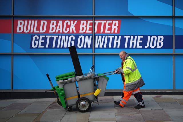 <p> A street cleaner walks past conservative party branding </p>