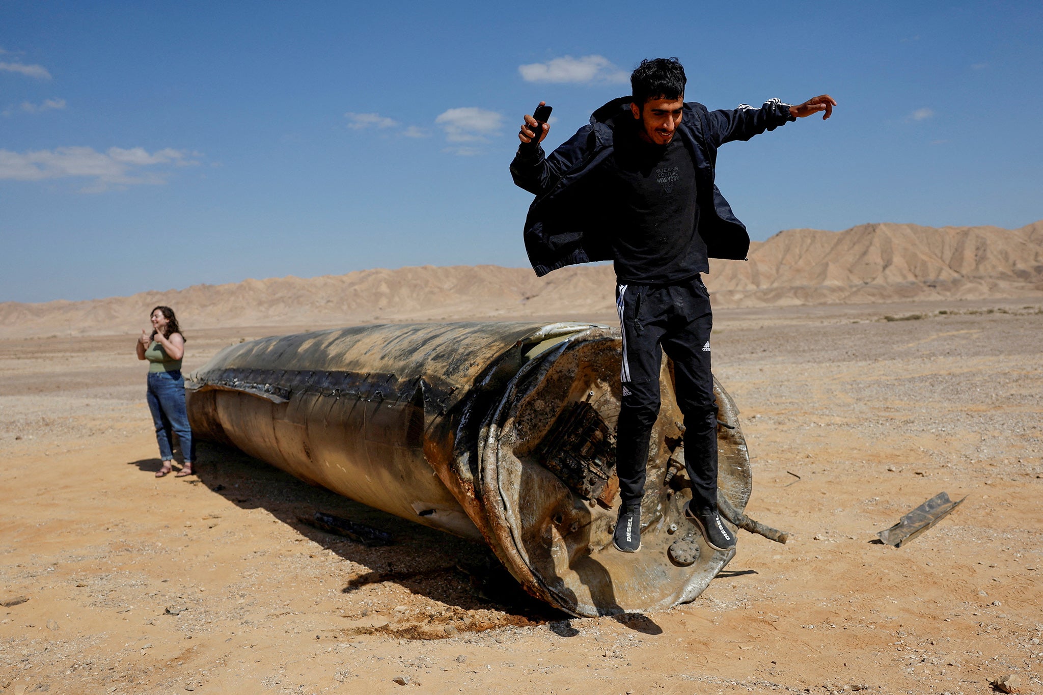 A man jumps off apparent remains of a ballistic missile lying in the desert, following an attack by Iran on Israel