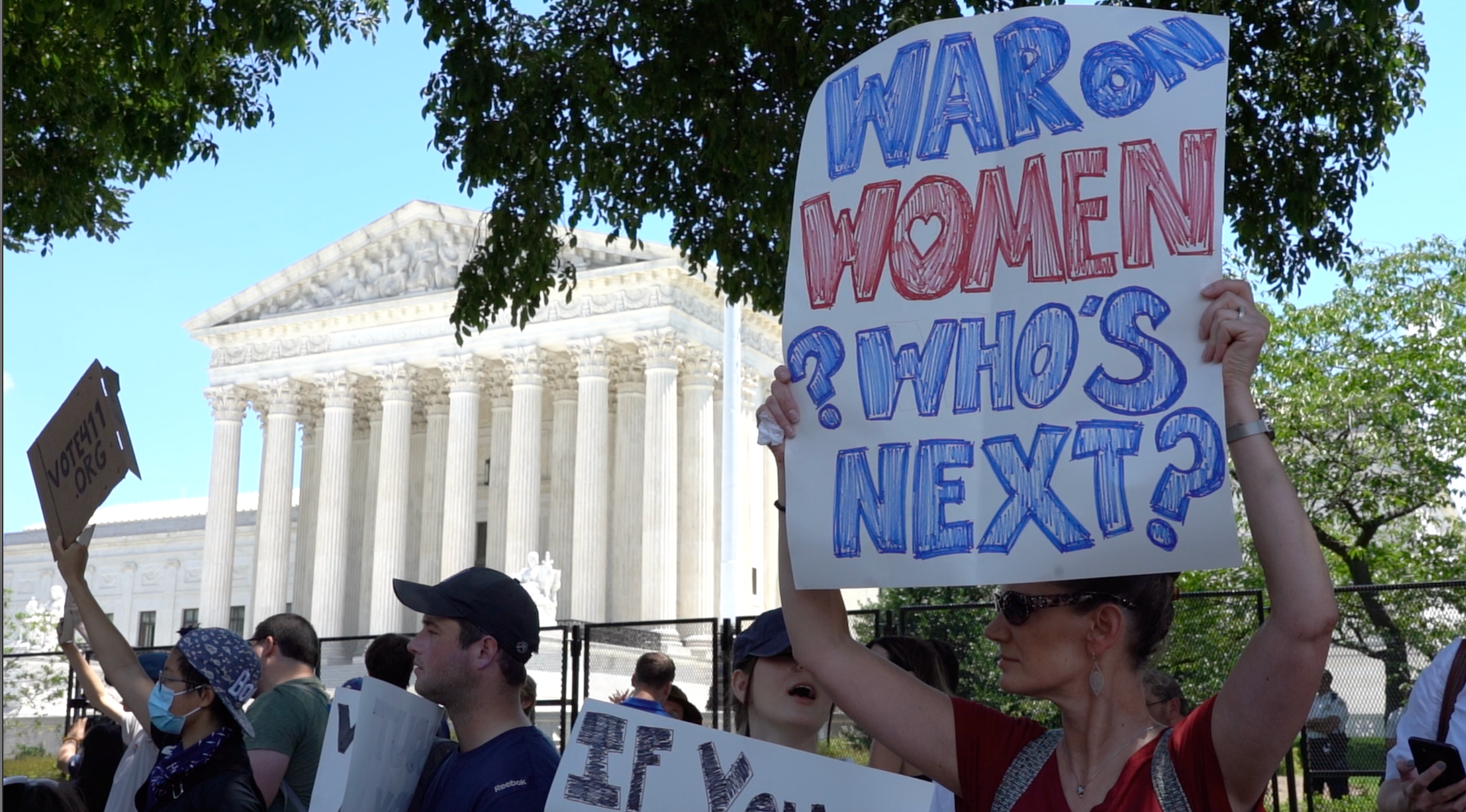 People protesting outside of the Capitol building in DC. A woman holds up a sign that reads: ‘War on women. Who’s next?’