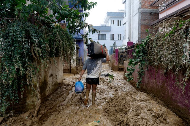 <p>File. A man walks through a muddy alleyway carrying belongings salvaged from his flooded house in Kathmandu, Nepal, on 30 September 2024</p>