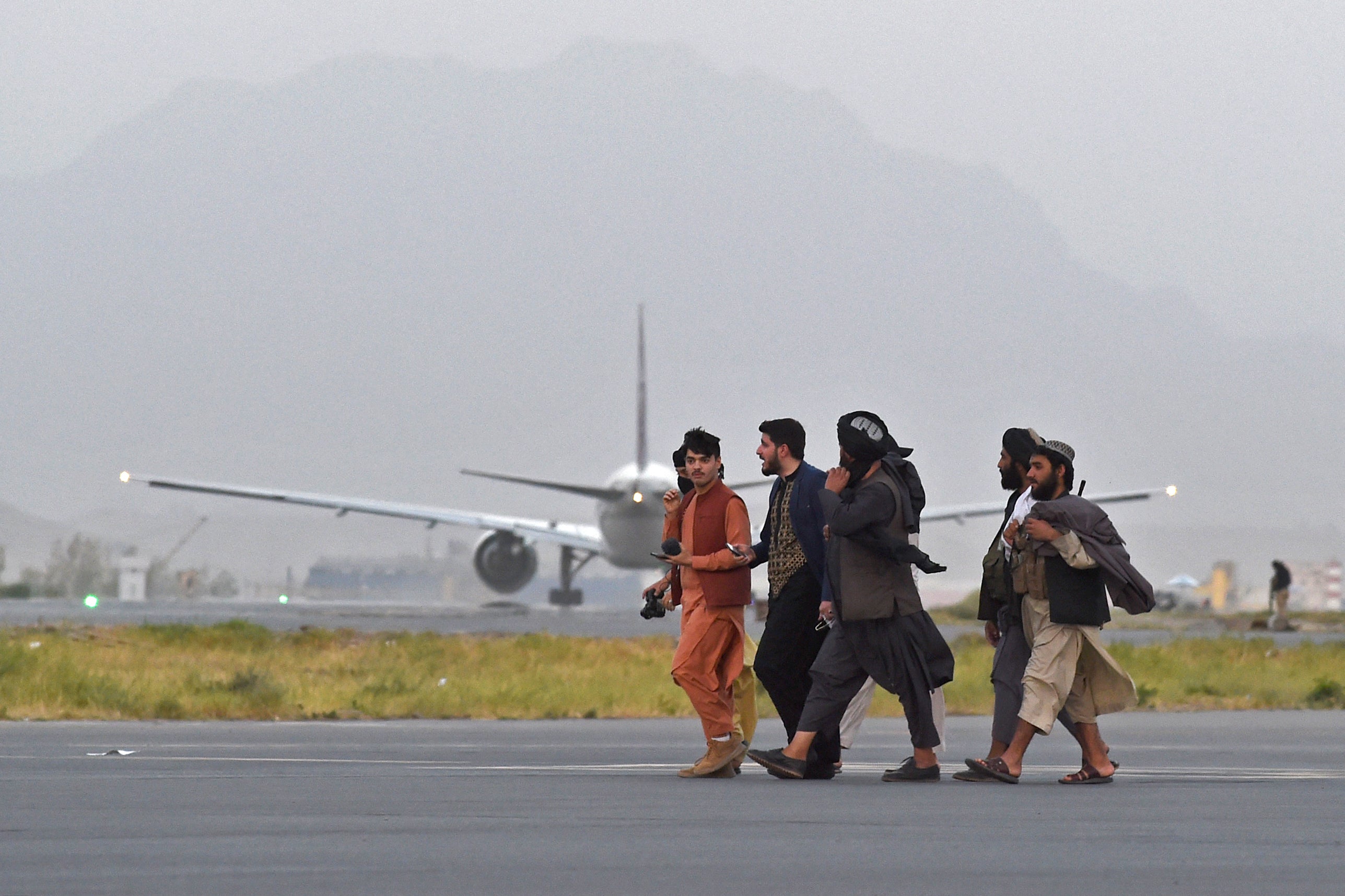 Taliban fighters walk past a Qatar Airways aircraft preparing to take off from the airport in Kabul