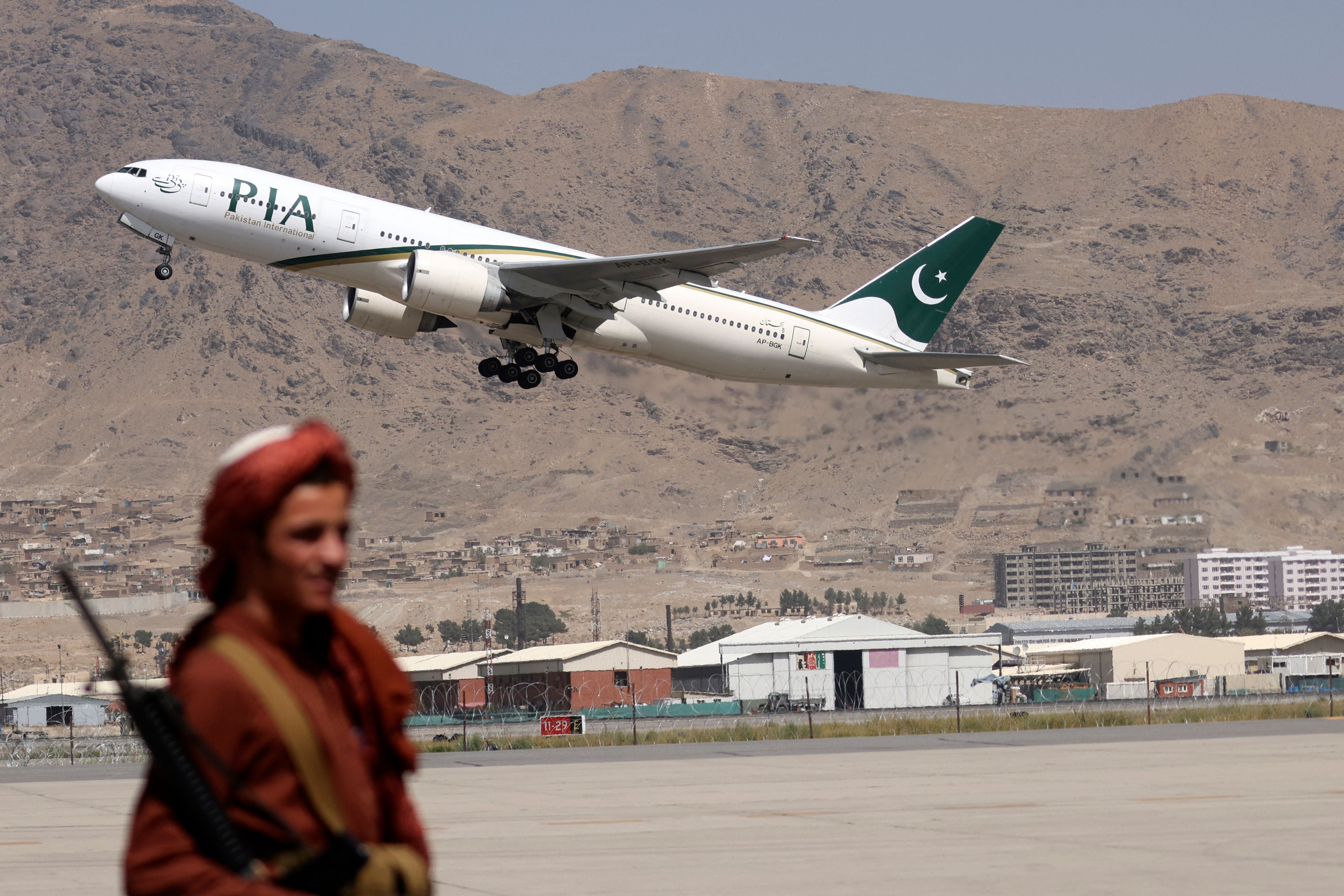 A Taliban fighter stands guard as a Pakistan International Airlines plane takes off