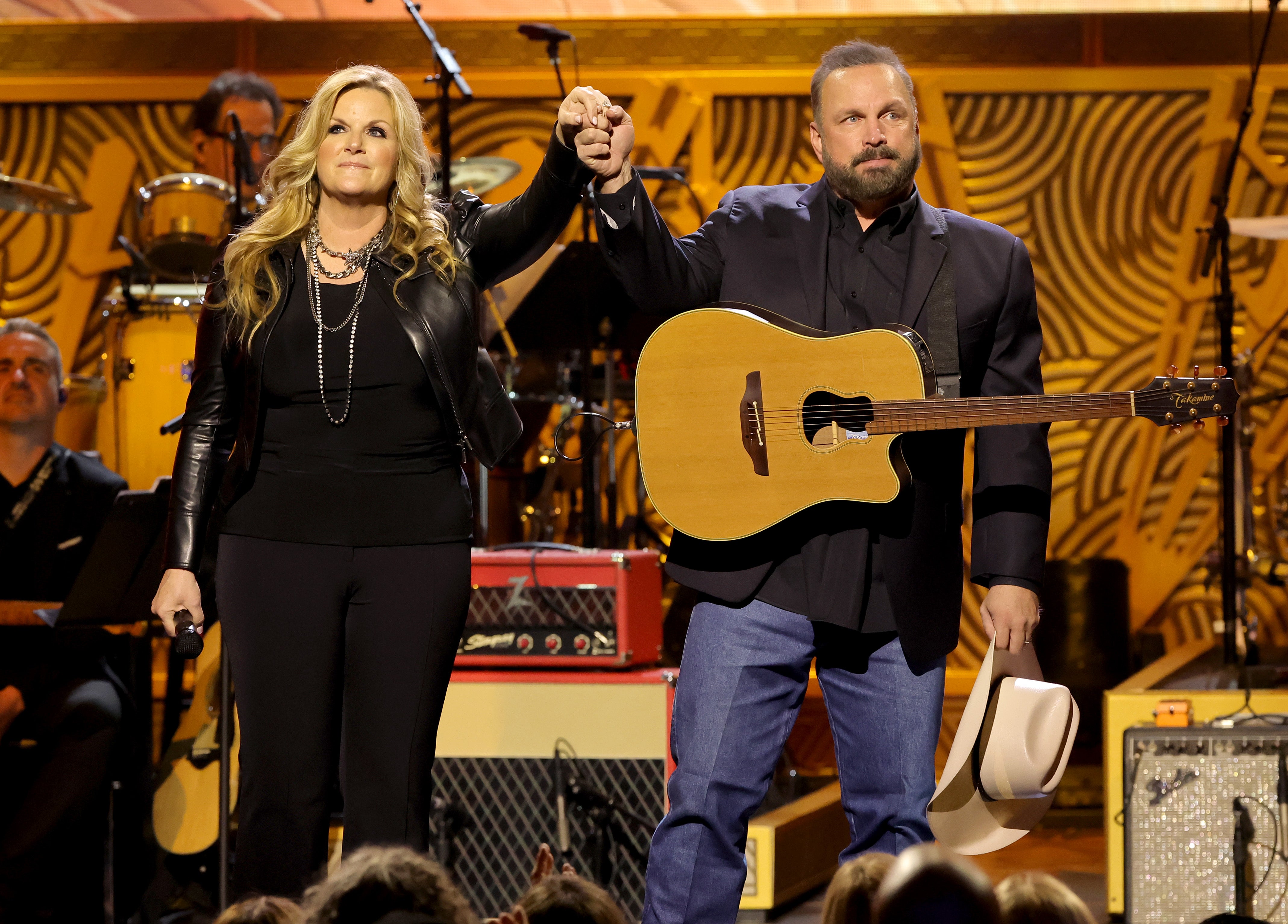 Garth Brooks e Trisha Yearwood de mãos dadas no palco. Brooks postou uma foto ao lado de Yearwood poucos dias antes de uma mulher identificada como Jane Roe entrar com uma ação alegando que a estrela da música country a estuprou em 2019.