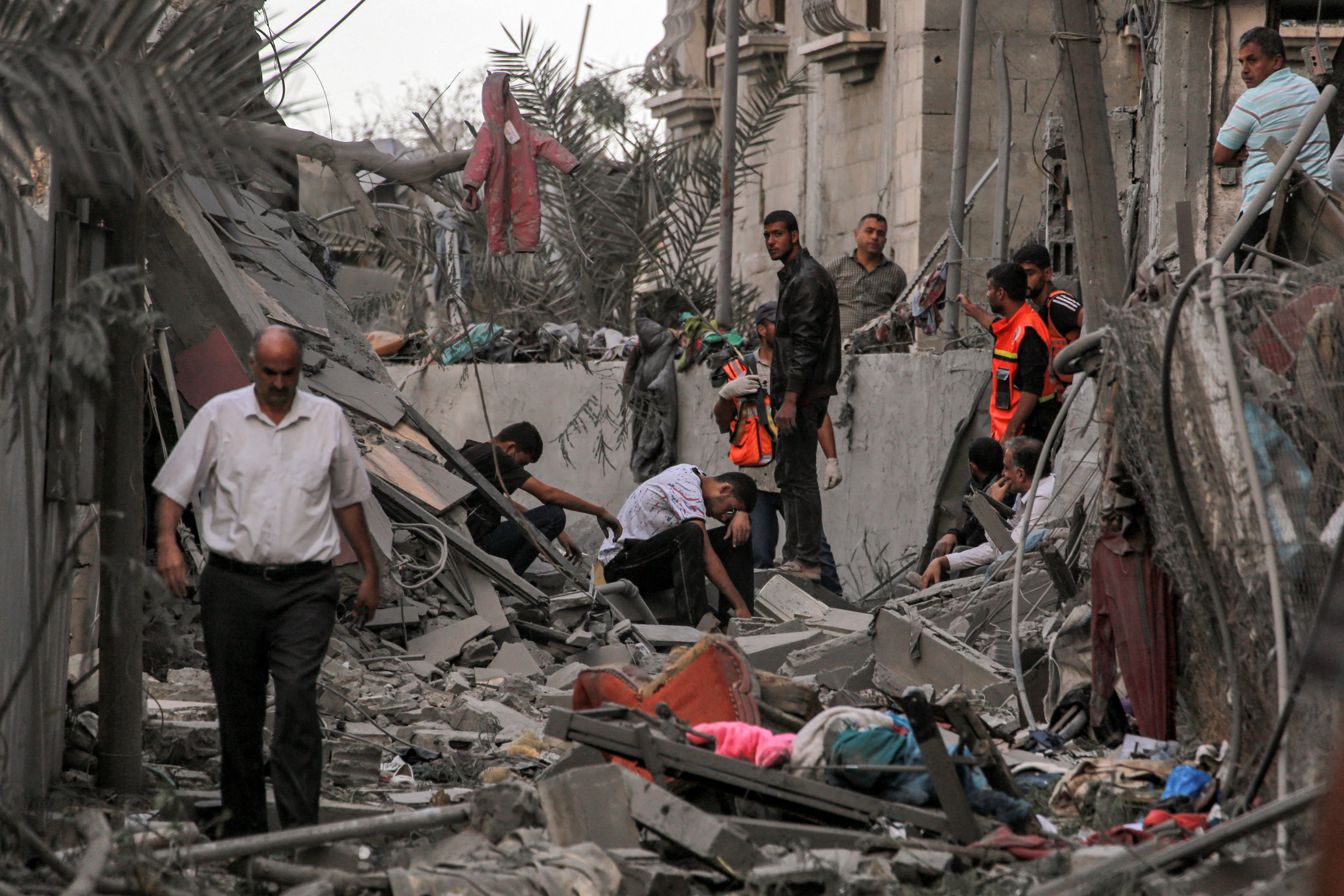 Palestinian Civil Defence rescuers and other people stand amidst debris by collapsed building in Khan Yunis in southern Gaza Strip on 2 October