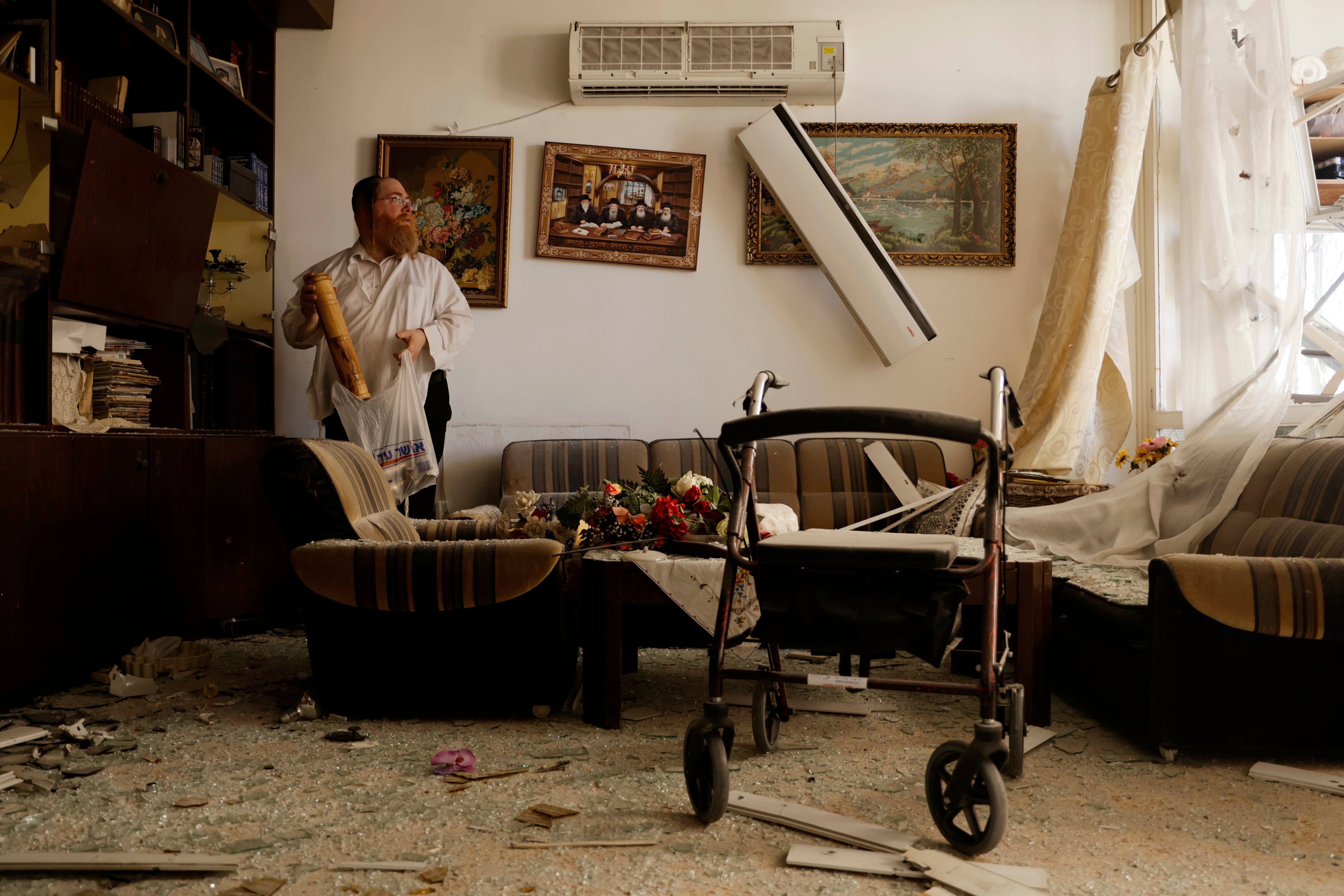 Crooked picture frames hang on the wall as an Israeli gathers his belongings in a carrier bag following a Hezbollah rocket attack near Haifa