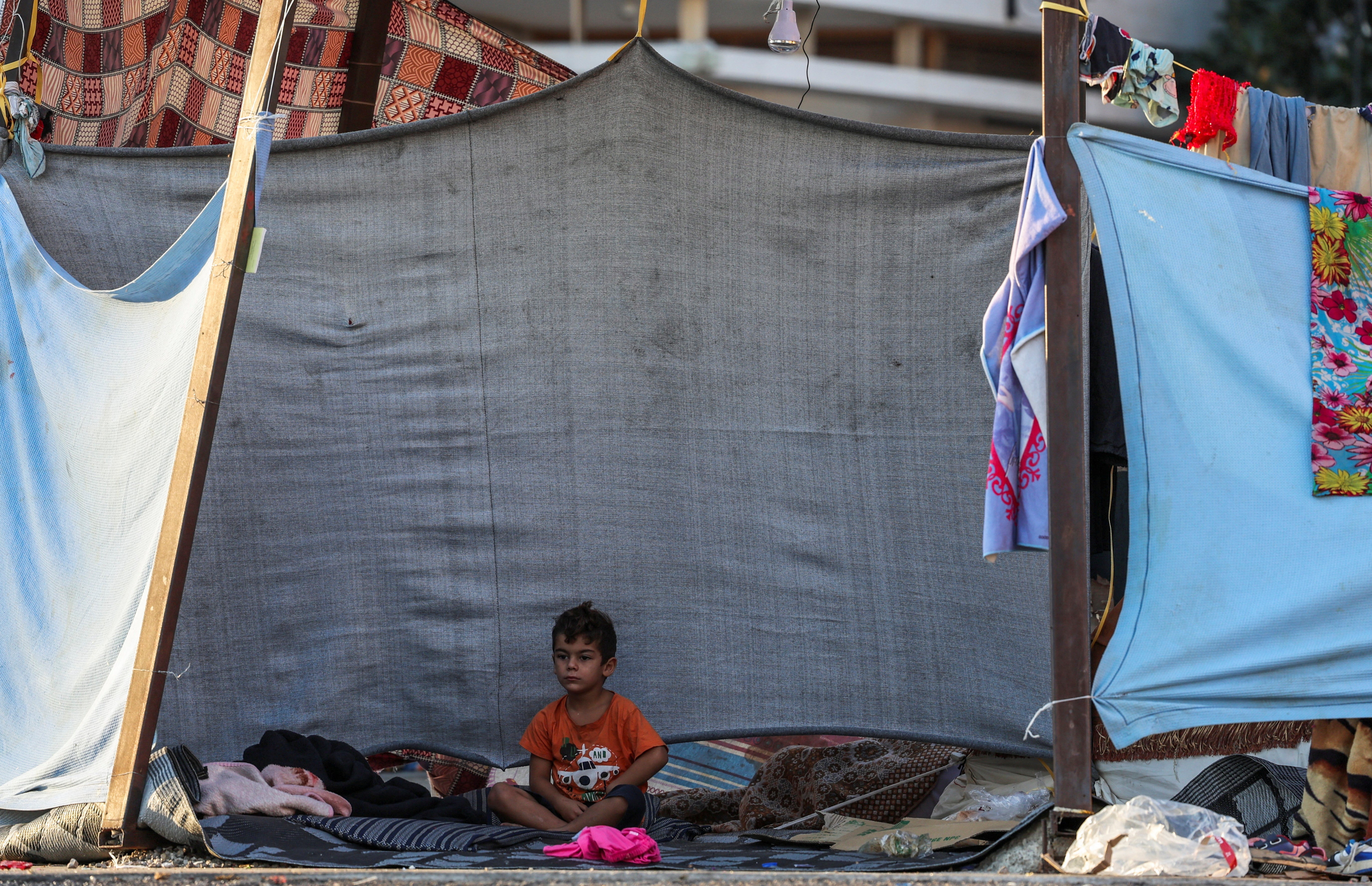 A young boy sits on a rug in front of a makeshift wall in central Beirut following intense Israeli airstrikes on city’s southern suburbs