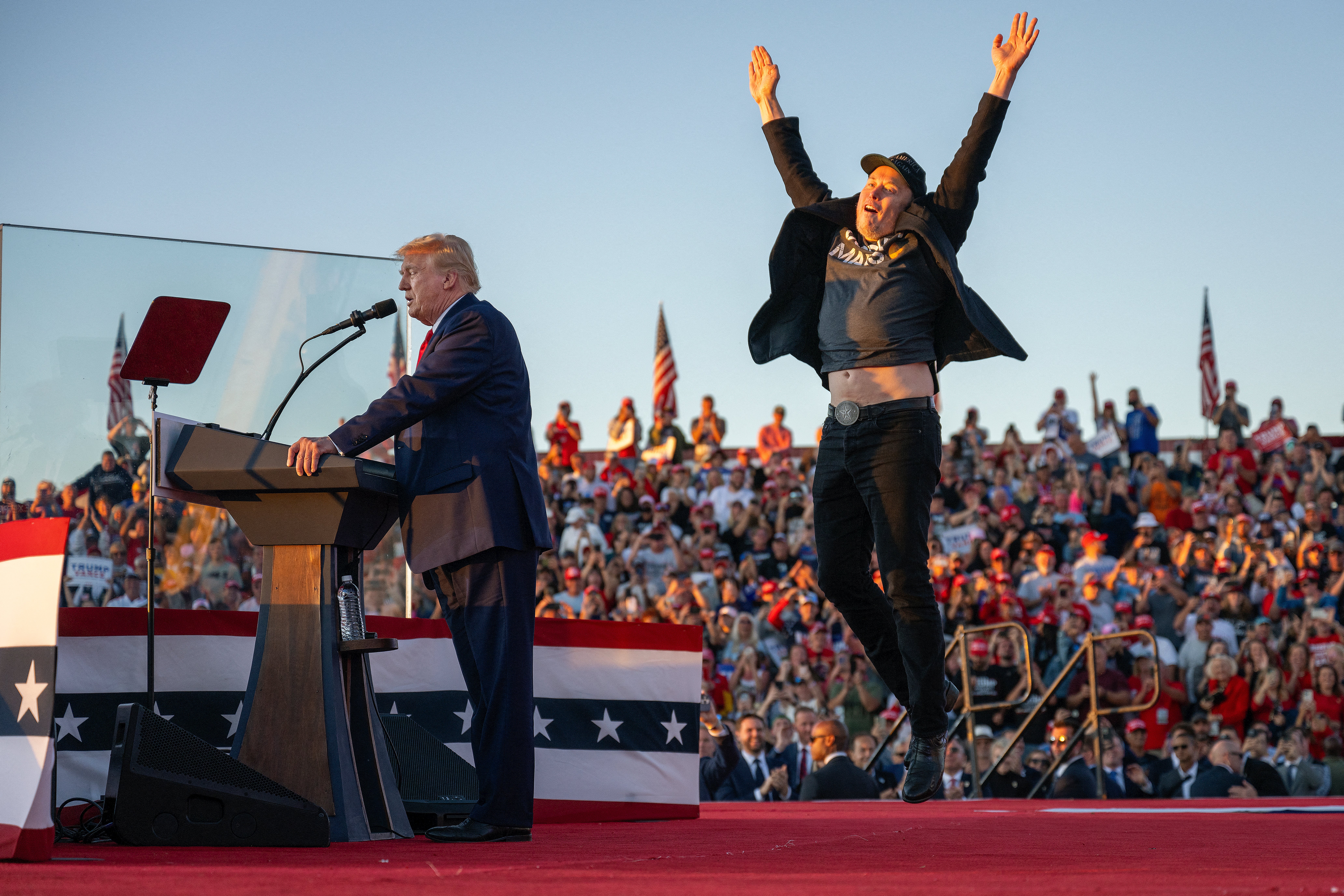 Tesla CEO Elon Musk (R) jumps on stage as he joins former US President and Republican presidential candidate Donald Trump during a campaign rally at site of his first assassination attempt in Butler, Pennsylvania