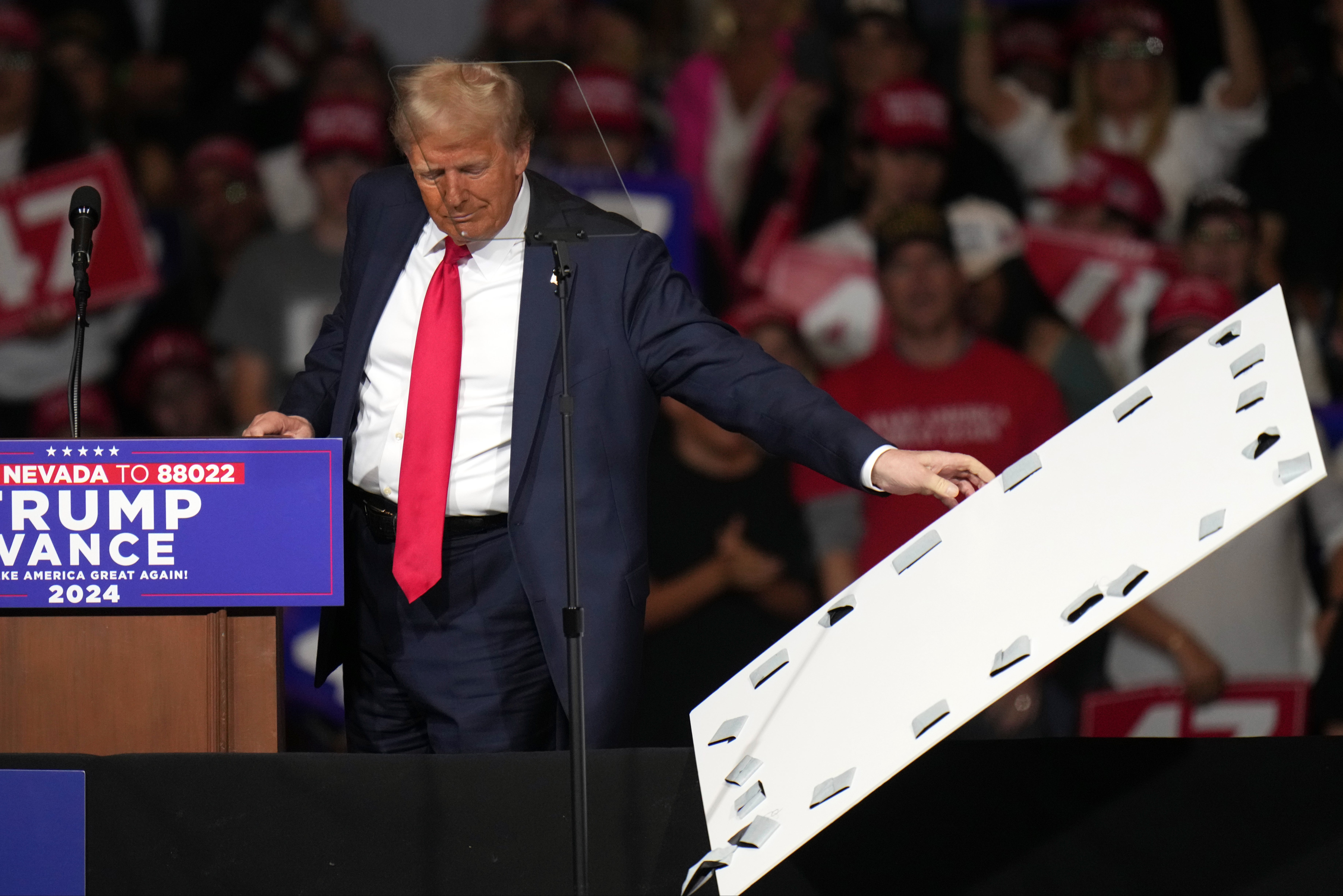 Republican presidential nominee former President Donald Trump picks up a cover that came off a protective barrier as he speaks at a campaign rally