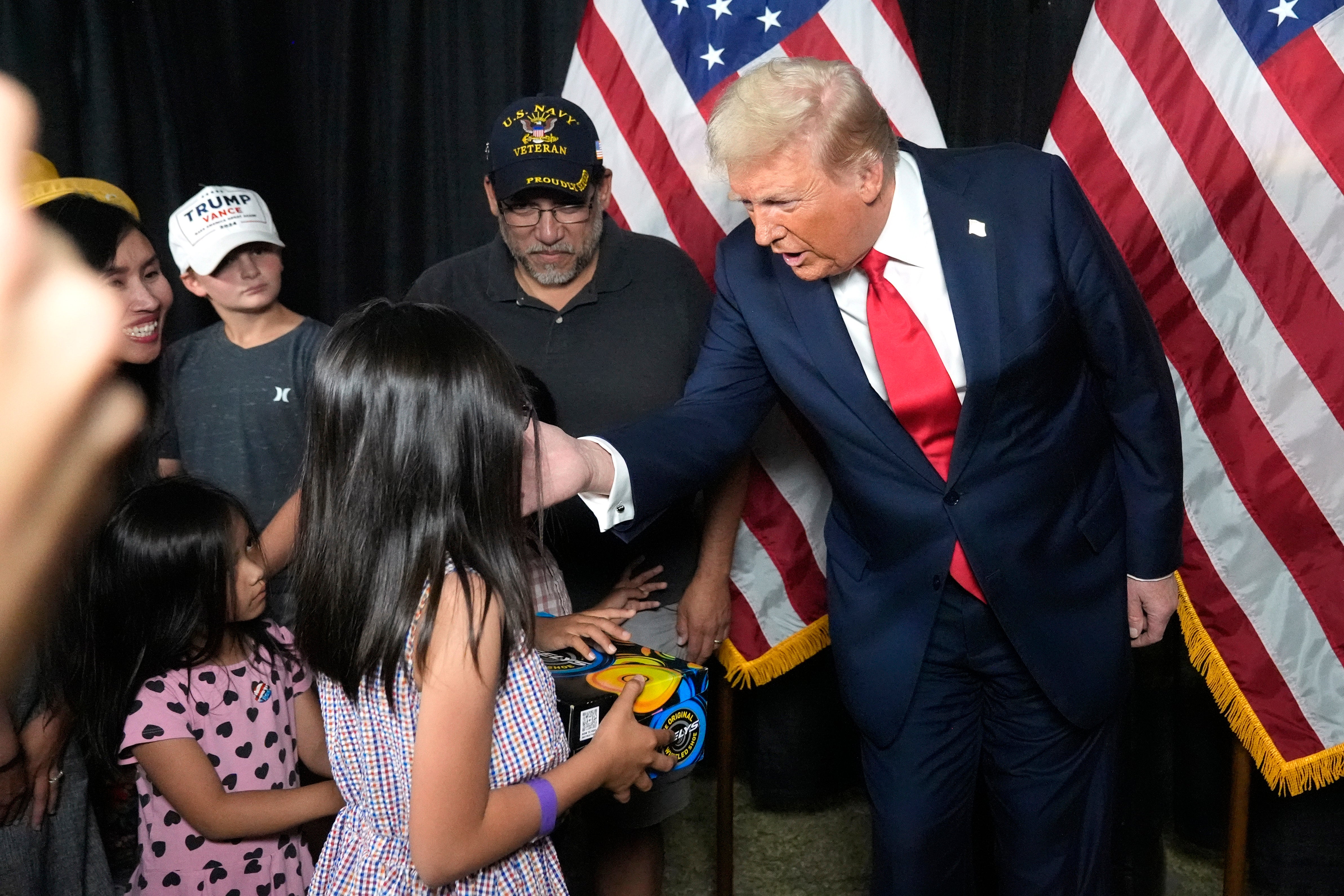 Republican presidential nominee former President Donald Trump, right, gives a young attendee a pair of shoes before he speaks at a campaign rally at the Calhoun Ranch, Saturday, Oct. 12, 2024, in Coachella, California