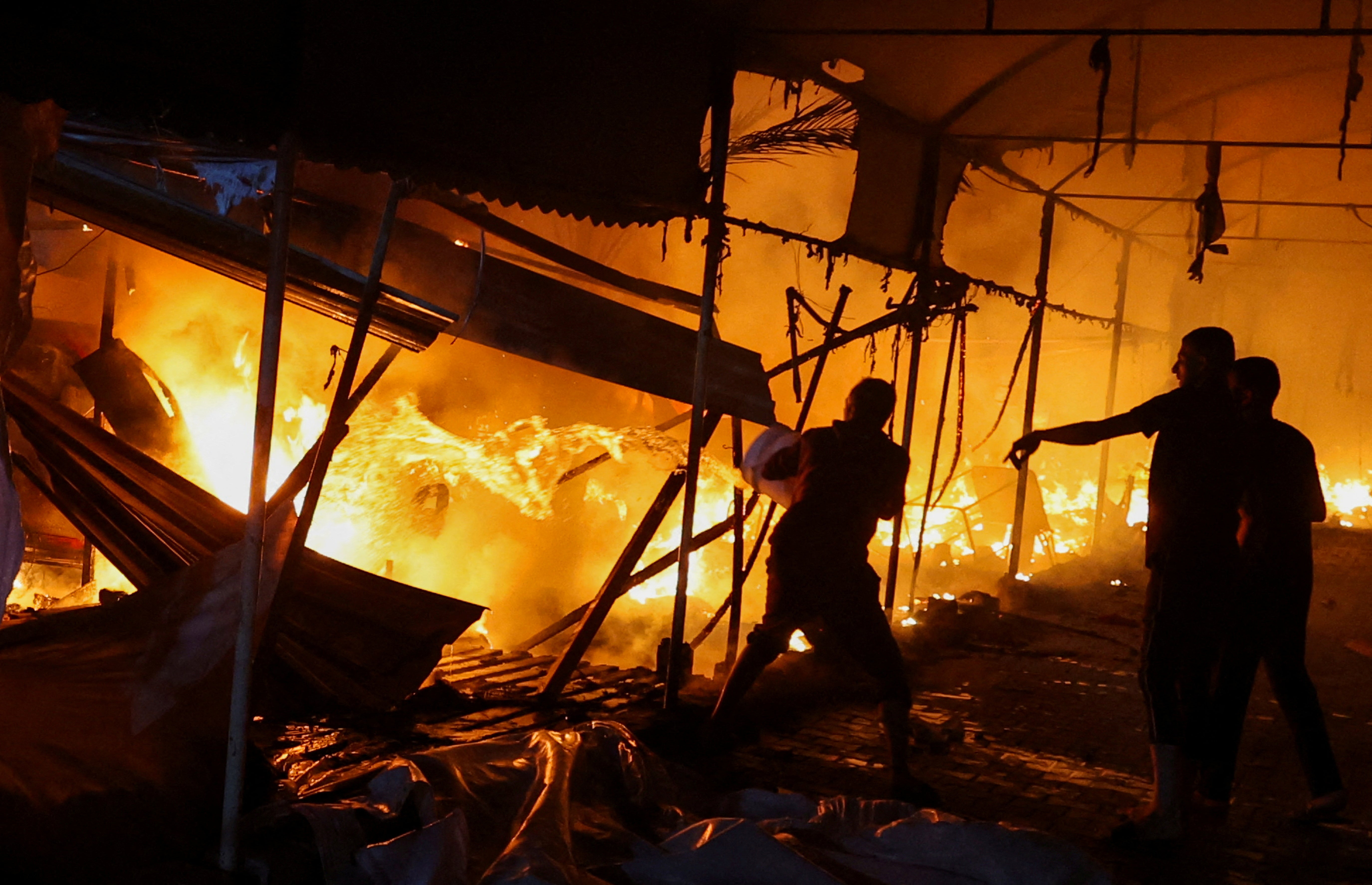 Three men attempt to extinguish a fire after an Israeli airstrike on tents sheltering displaced people