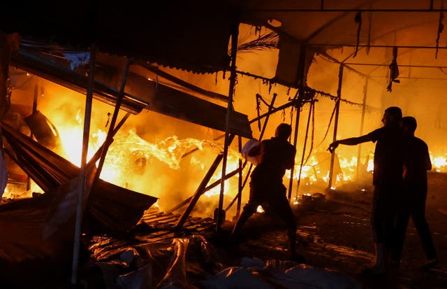 <p>Three men attempt to extinguish a fire after an Israeli airstrike on tents sheltering displaced people</p>