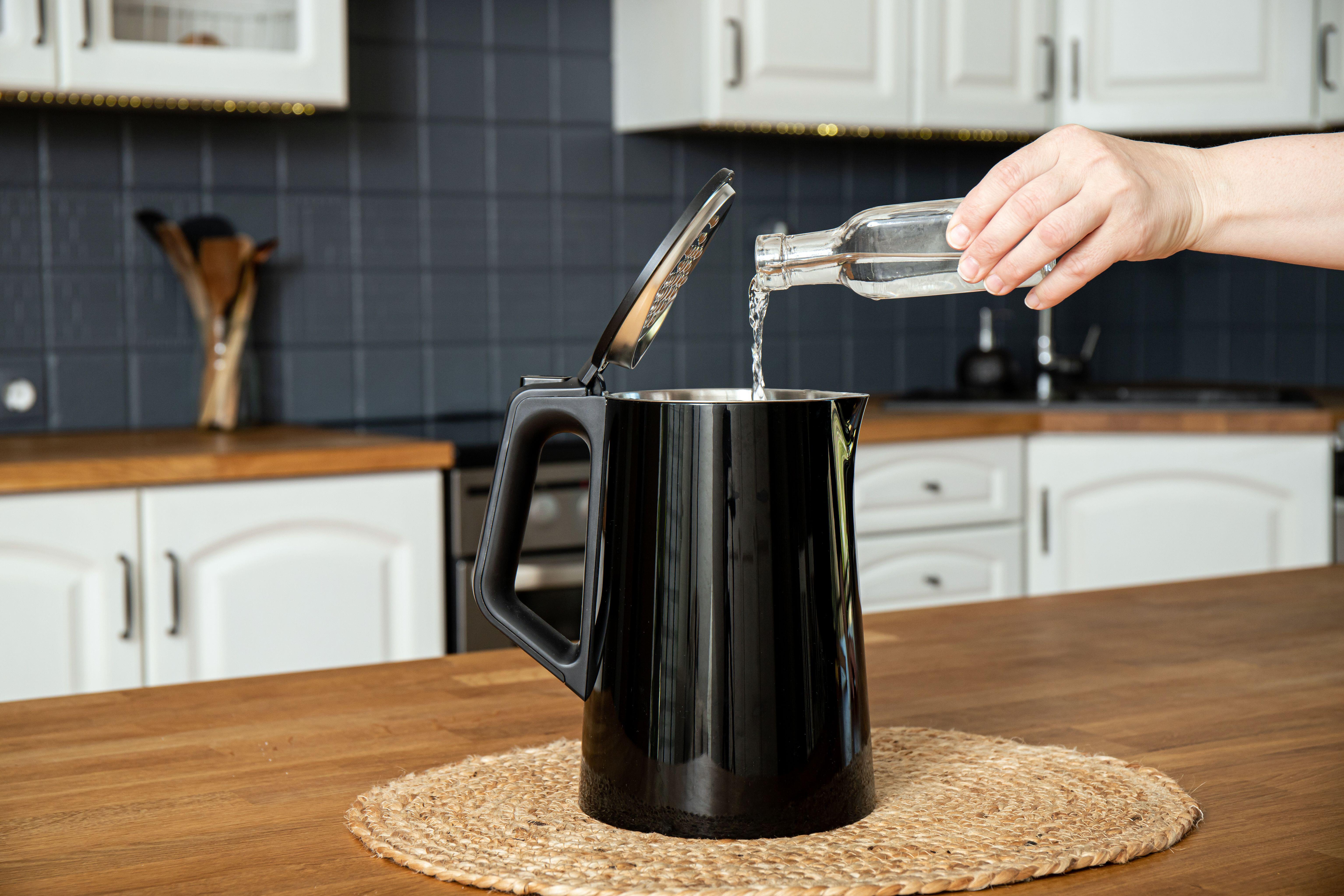 Woman pouring natural destilled acid white vinegar in electric kettle to remove boil away the limescale