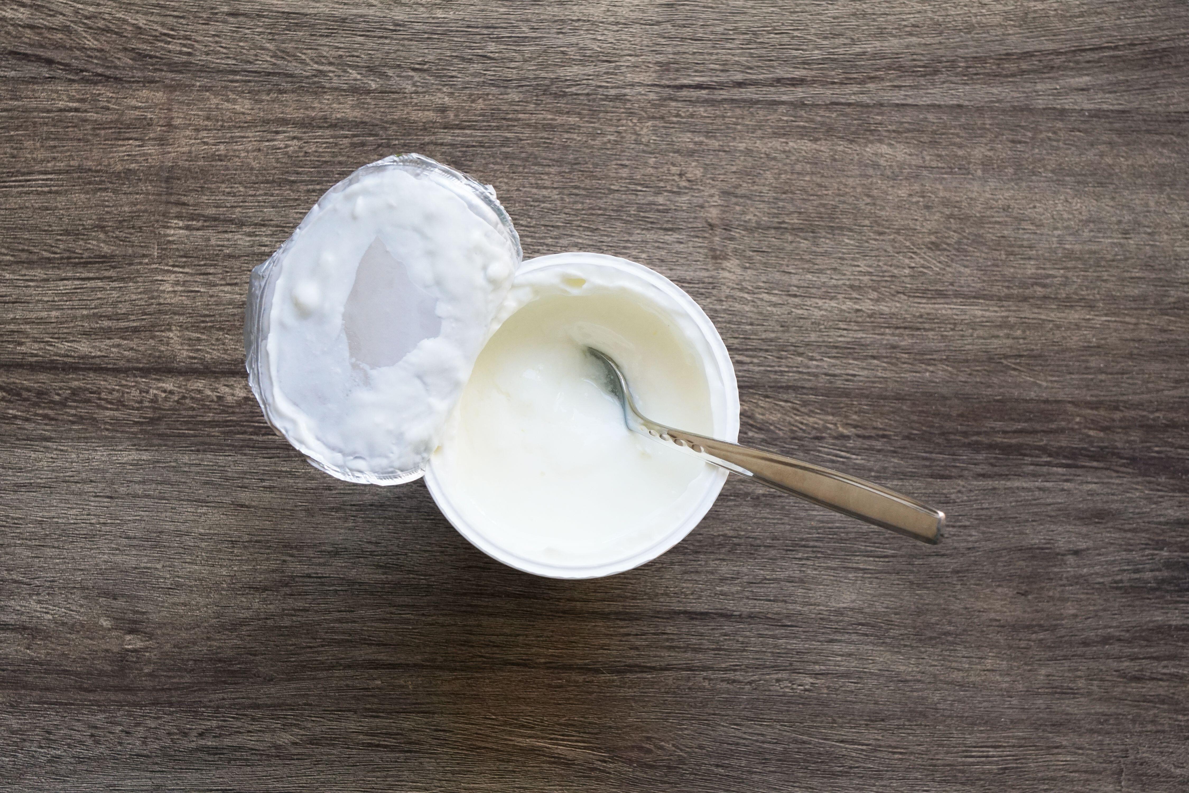 Overhead view of pot of natural yoghurt with a spoon in