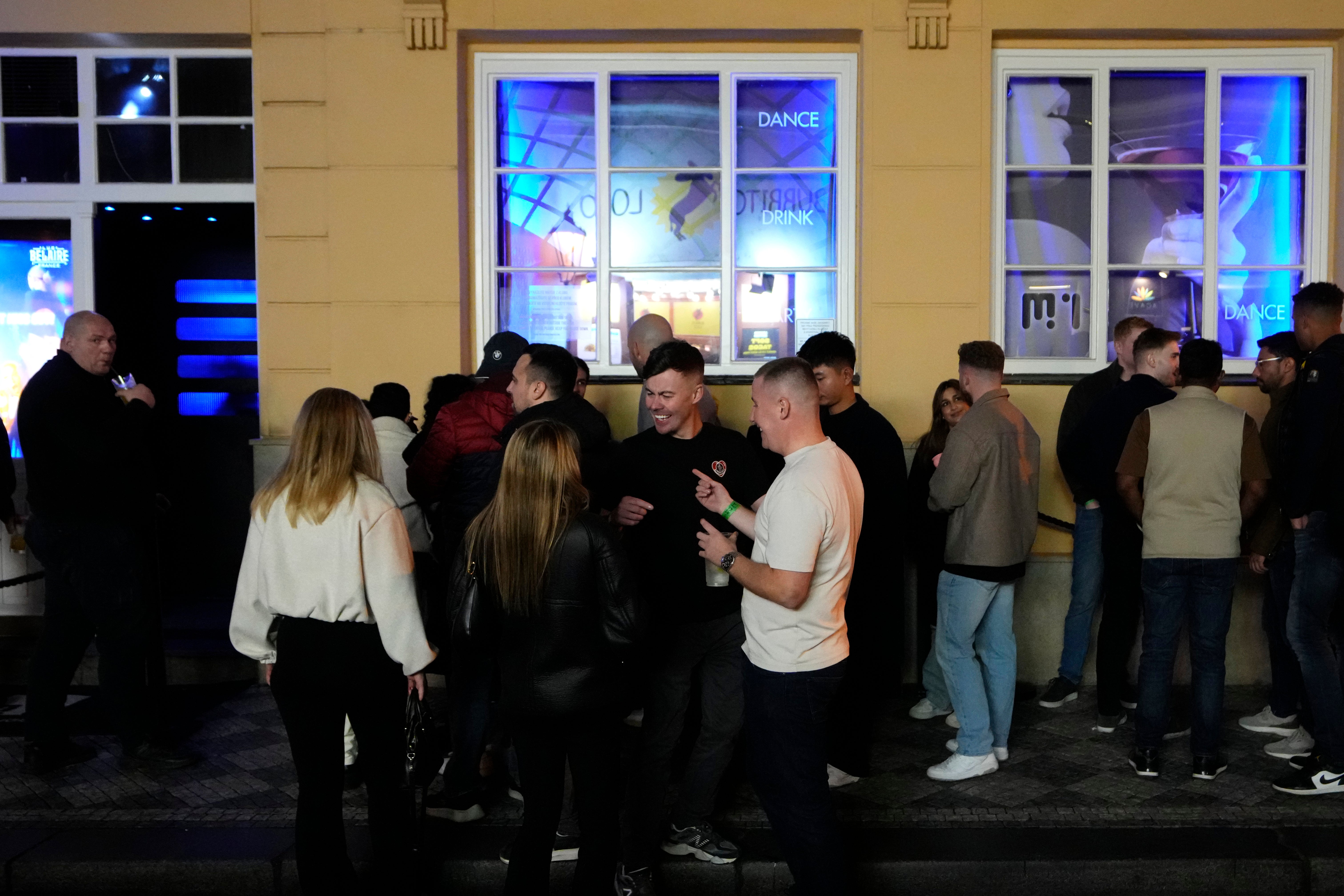 A group of tourists stand in line outside a bar as they attend a pub crawl tour in downtown Prague