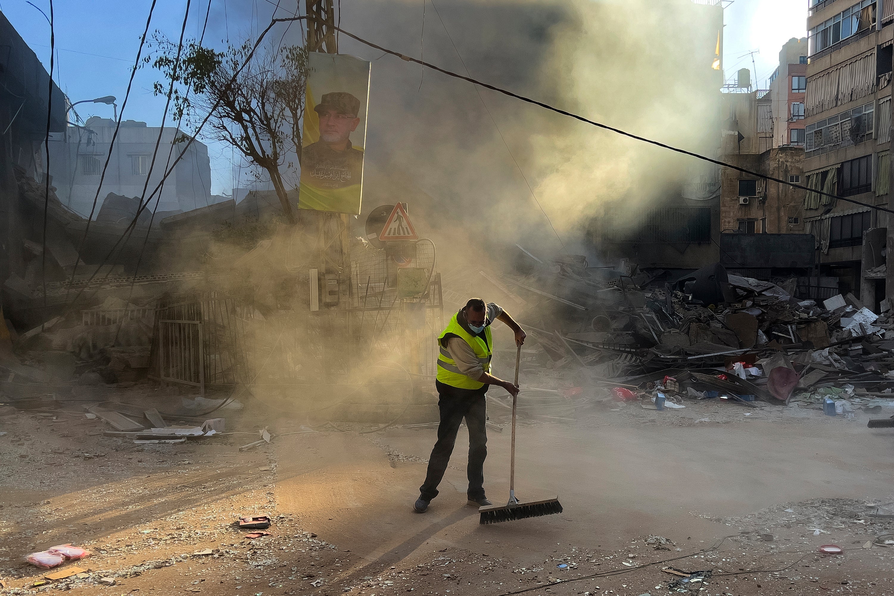 A worker cleans a street as smoke rises from a destroyed building hit by an Israeli airstrike in Dahiyeh earlier on Sunday