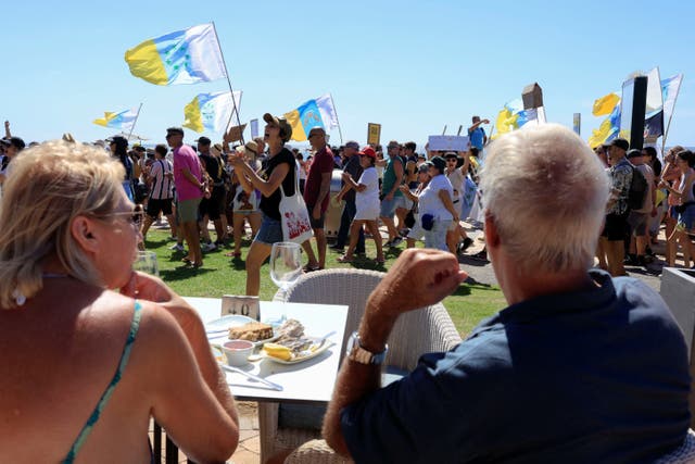 <p>A couple of tourists sitting on a terrace watch a demonstration for a change in the tourism model in the Canary Islands</p>