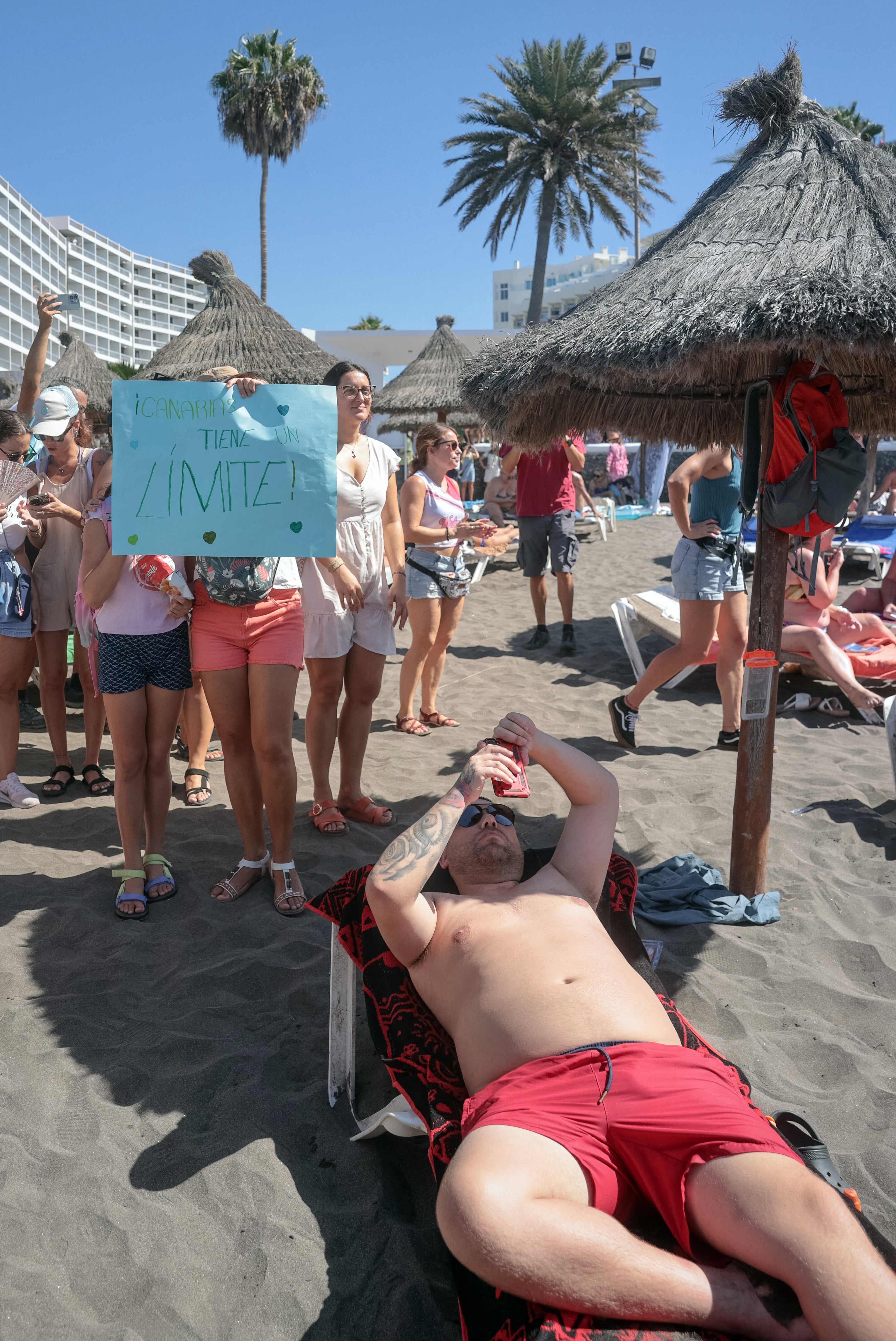 A sunbather remains unfazed as a protester holds a sign reading ‘The Canary Islands have a limit’