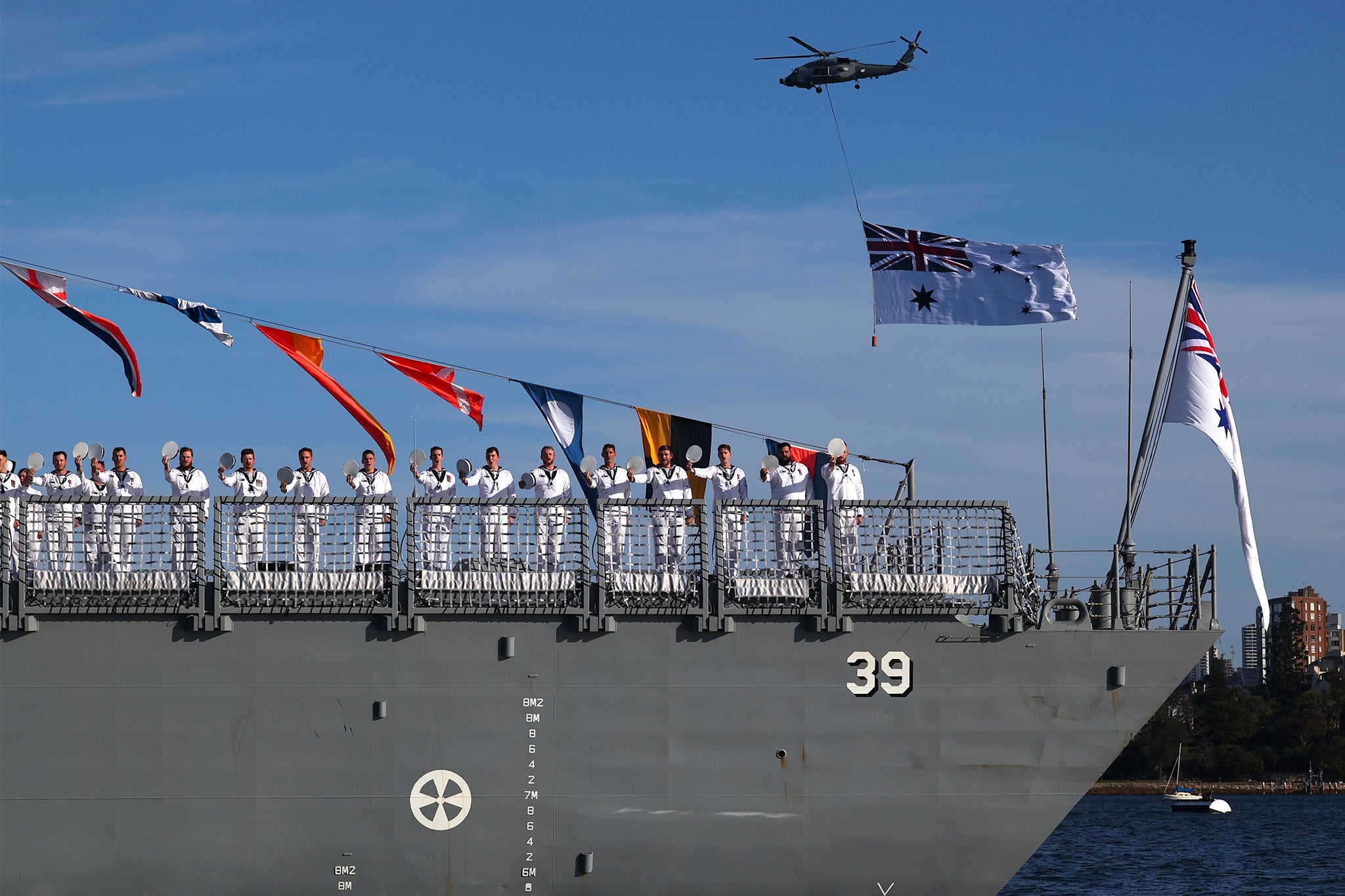 Bemanningsleden van de HMAS Hobart van de Royal Australian Navy groeten terwijl koning Charles III en koningin Camilla een vlootonderzoek van de Australische marine uitvoeren in de haven van Sydney.