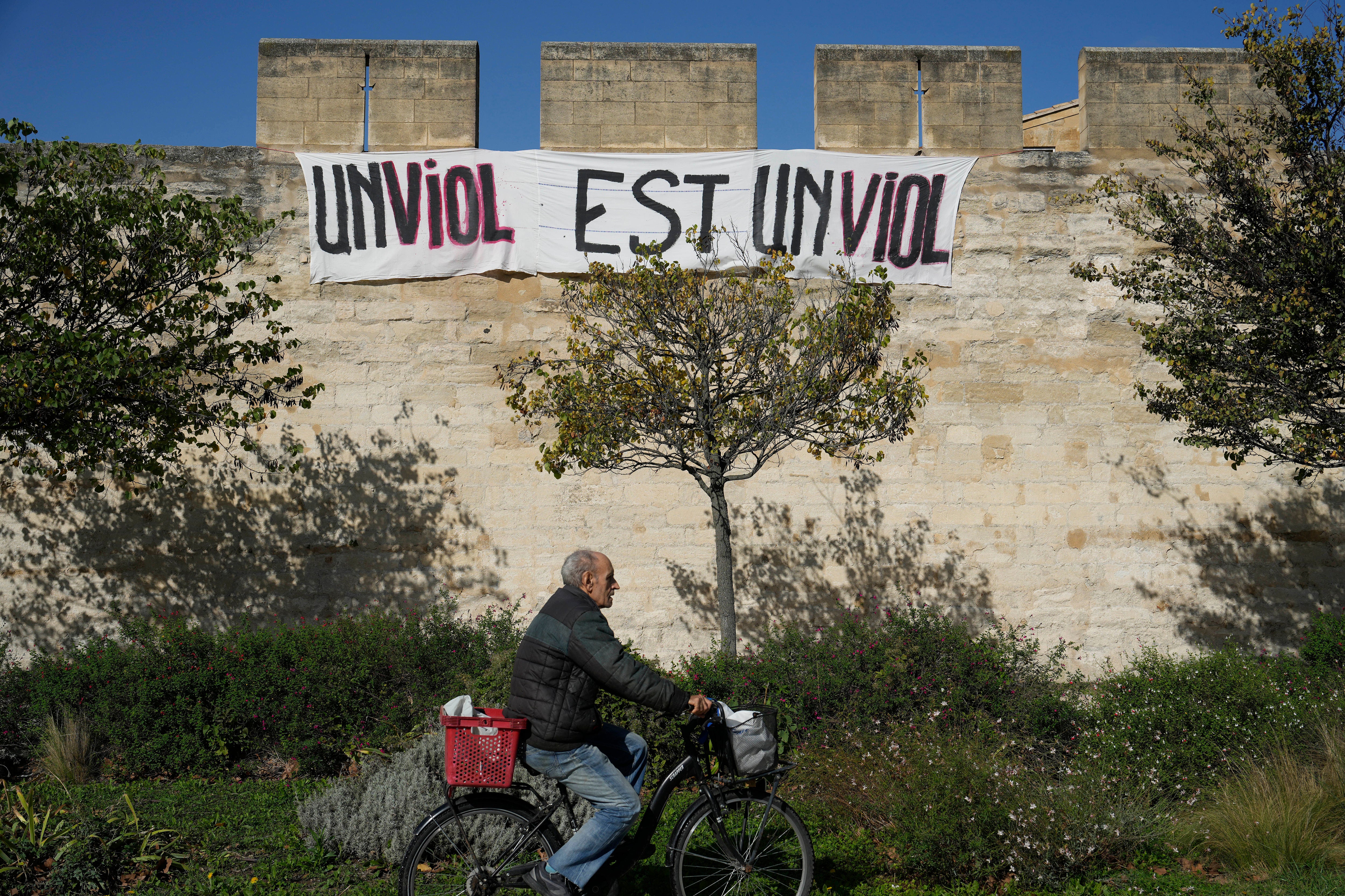 A man rides a bicycle in front of a banner reading: ‘A rape is a rape,’ in Avignon, southern France