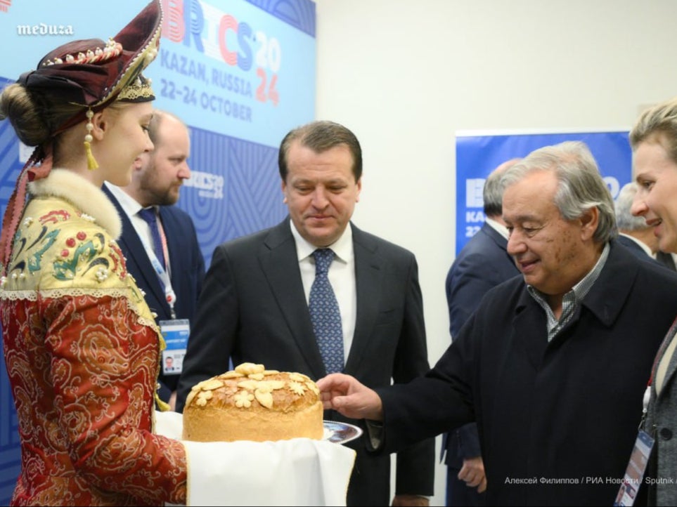 Antonio Guterres (R) eats some cake presented by a woman at the entrance to BRICS 2024 in Kazan, Russia