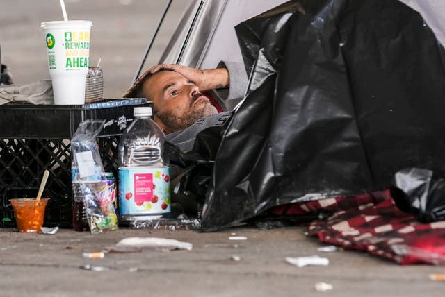 <p>A man in a homeless encampment lays among possessions after Louisiana State police gave instructions for them to move to a different pre-designated location as they perform a sweep in advance of a Taylor Swift concert in New Orleans</p>