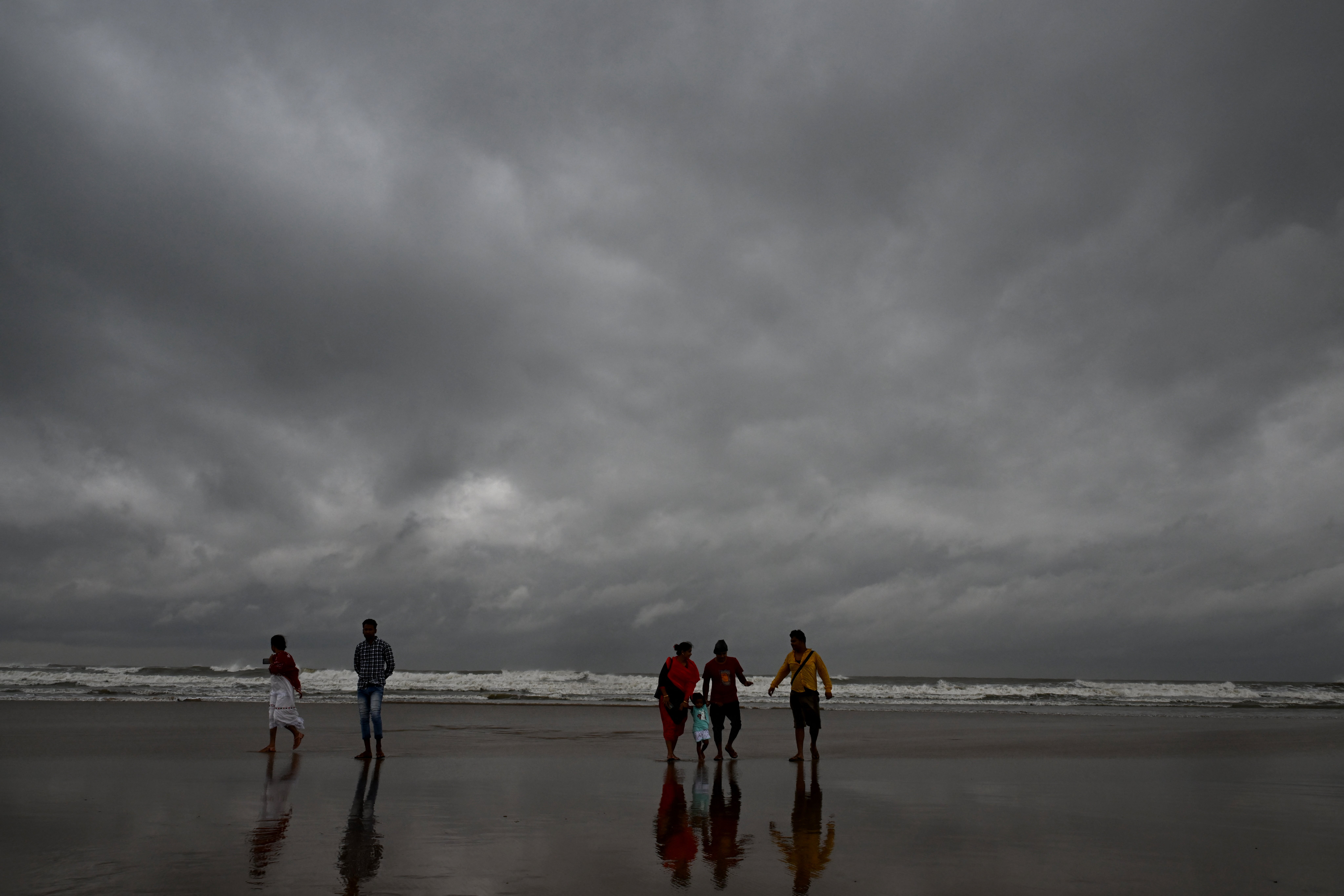 Dark clouds loom over the sea as local people and tourists walk along a beach in Digha, around 200km southwest of Kolkata