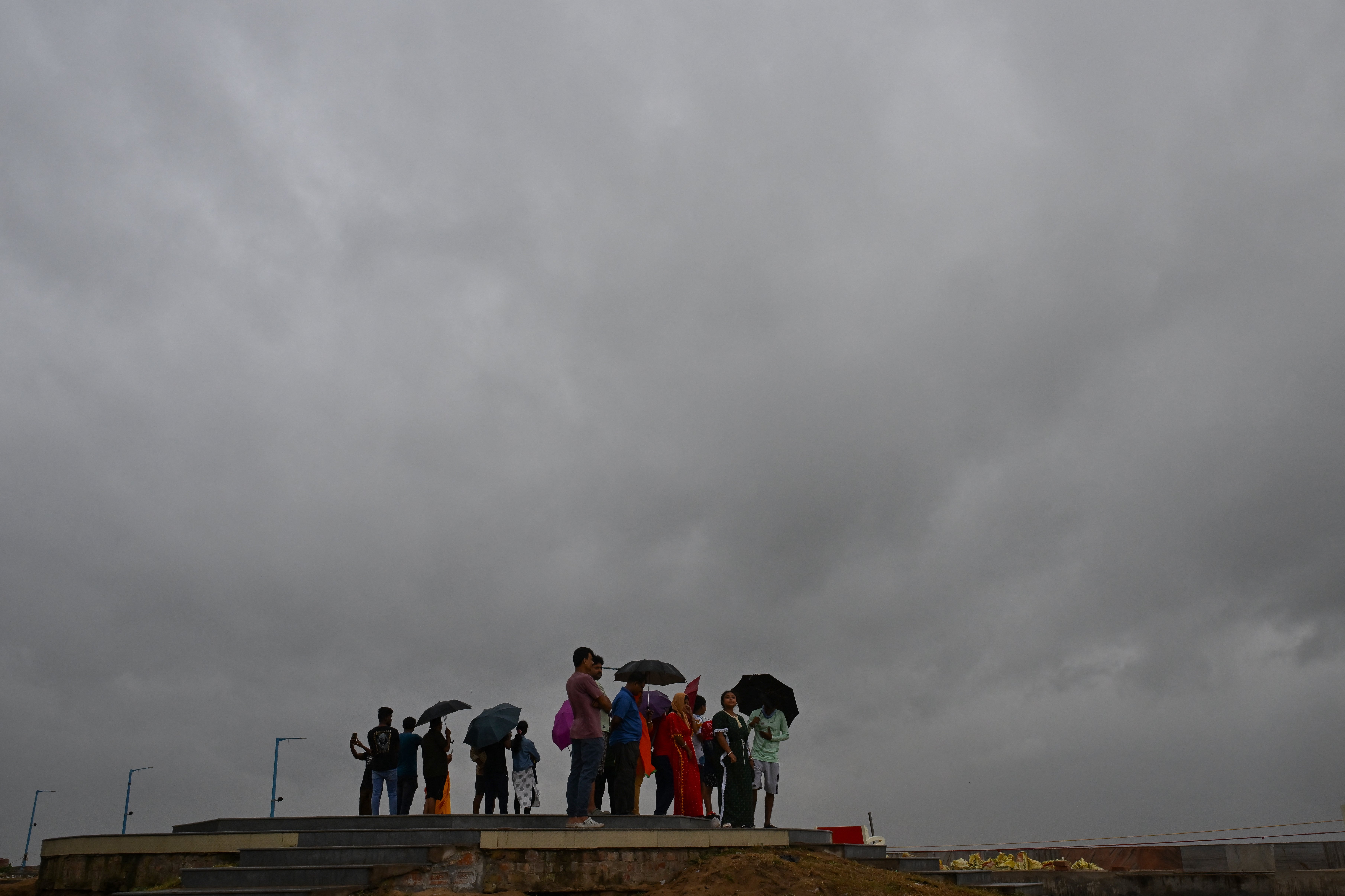 Dark clouds loom over the Bay of Bengal as local people and tourists stand along a beach in Digha