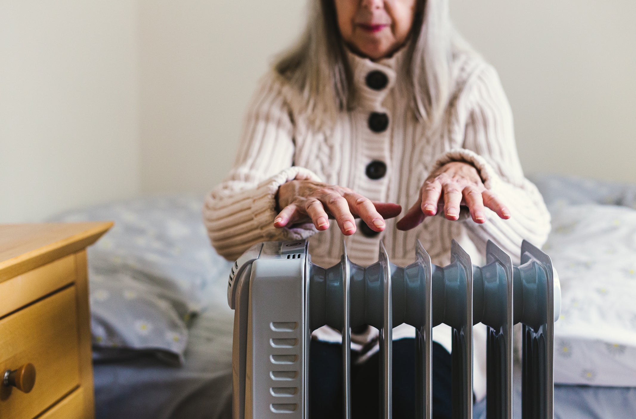 A retired senior woman in her 70s sits at home inside her cold house in winter (stock image)