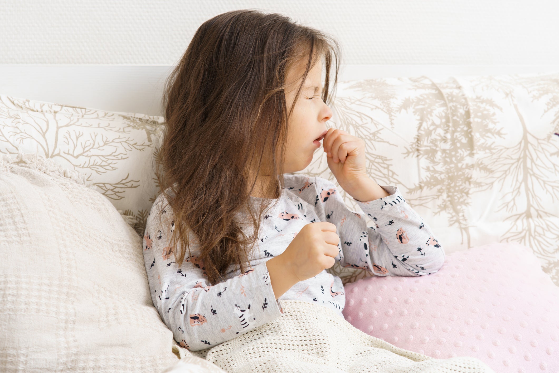 A little girl coughs in bed. More young children are being infected with walking pneumonia this year, as infections have spiked around the country