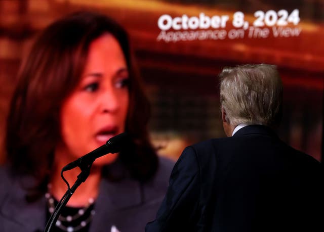 <p>Donald Trump watches as a video of his opponent, Kamala Harris, is played onscreen at his rally in Reno, Nevada, on October 11</p>