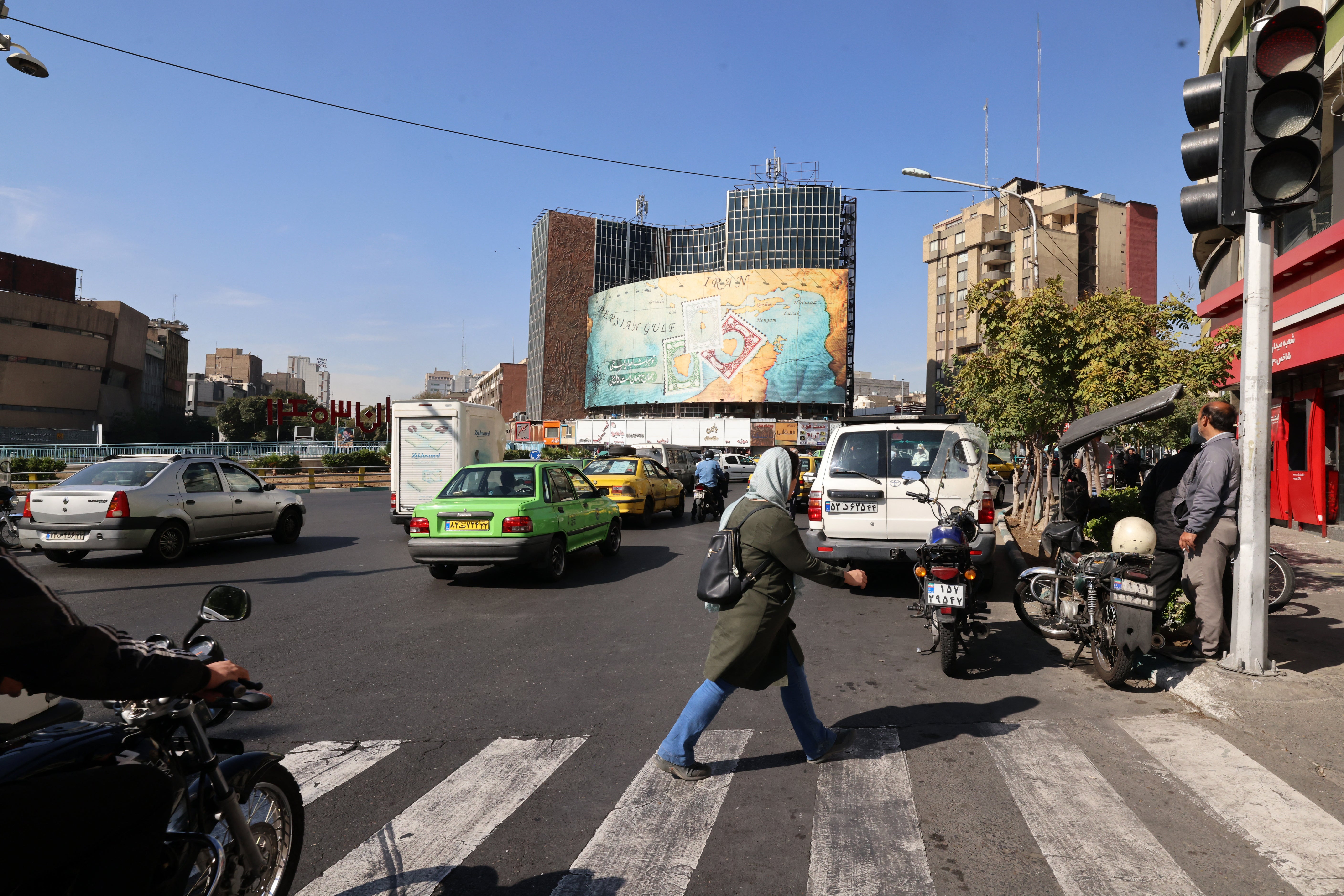 People walk and drive past a billboard covering the facade of a building on Vali-Asr square in Tehran