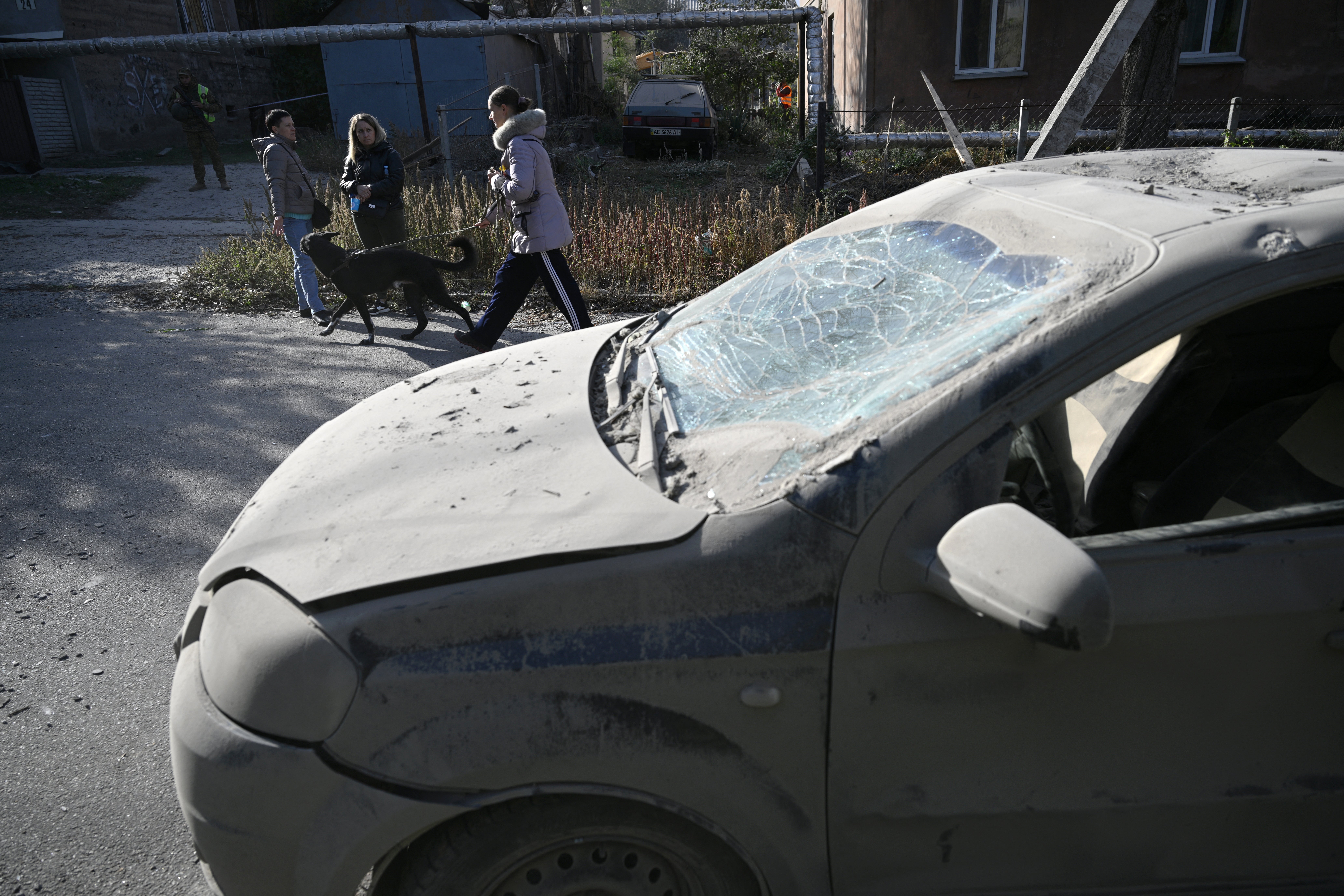 A local resident walks her dog near a damaged car on the site of a Russian missile strike in Dnipro, eastern Ukraine, on 26 October 2024