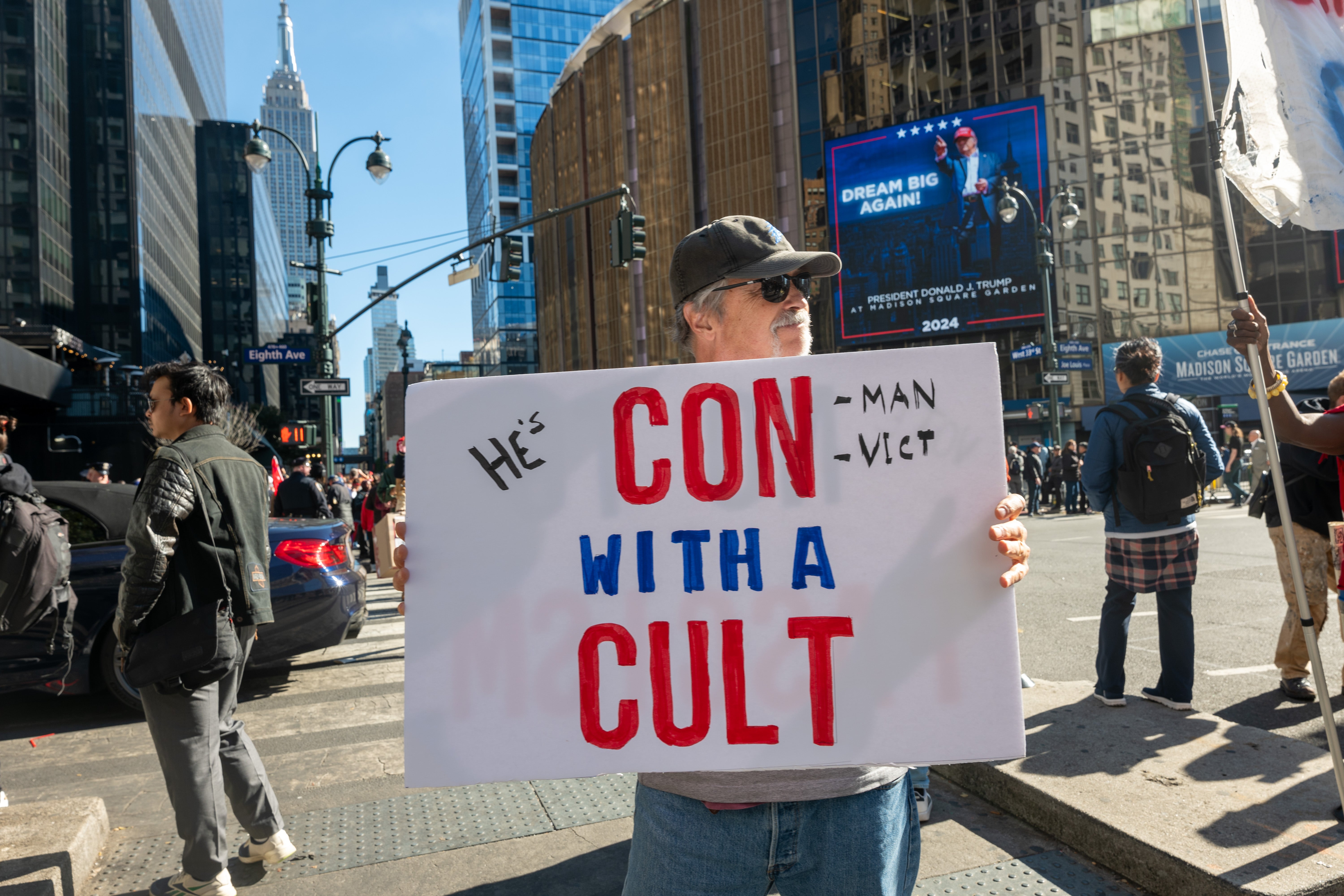 An anti-Trump protestor holds a sign that says, ‘Con with a cult’ outside of MSG where hundreds of Trump supporters are lined up