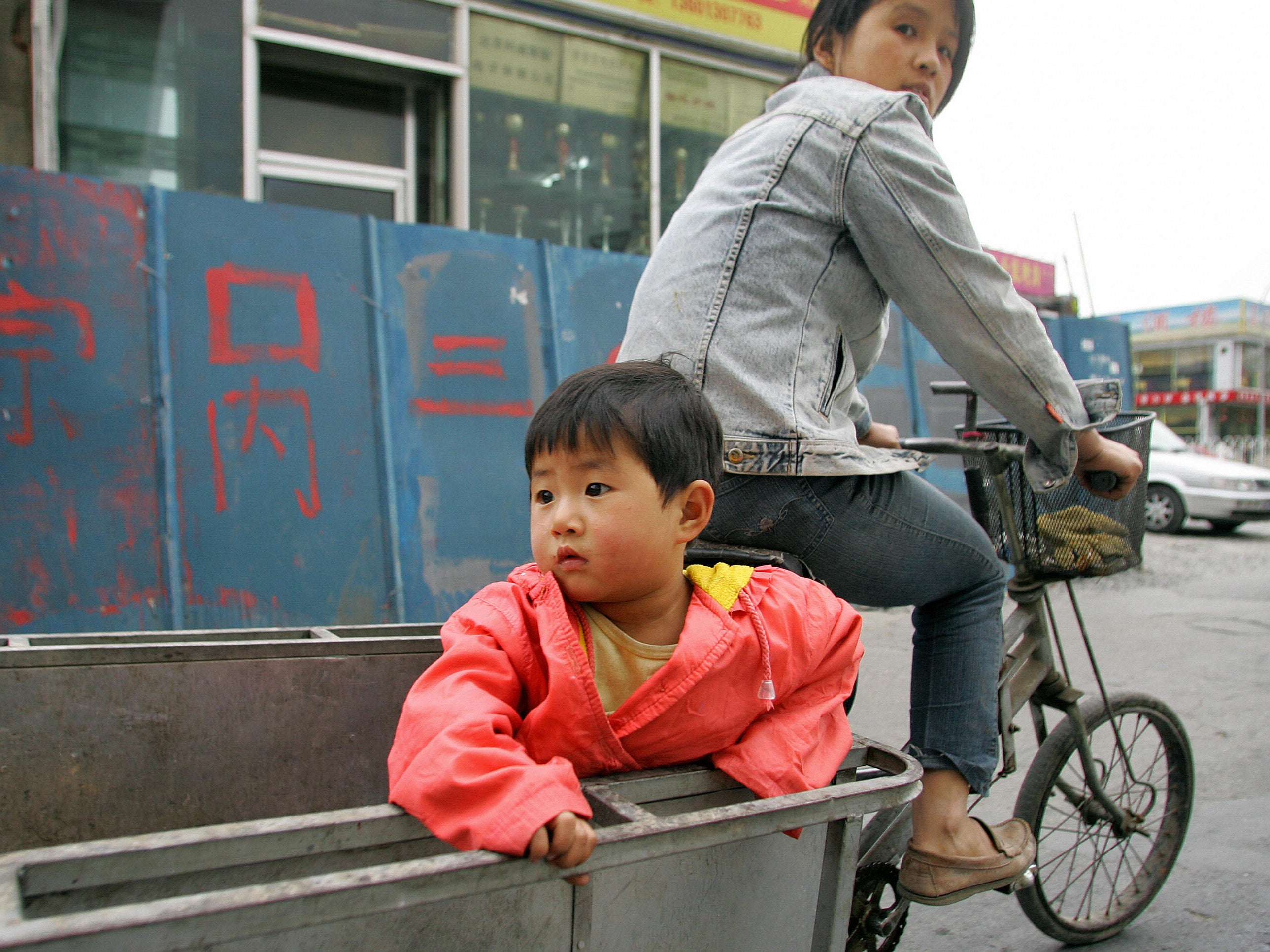 A child holds on while riding on the back of a tricycle in Beijing