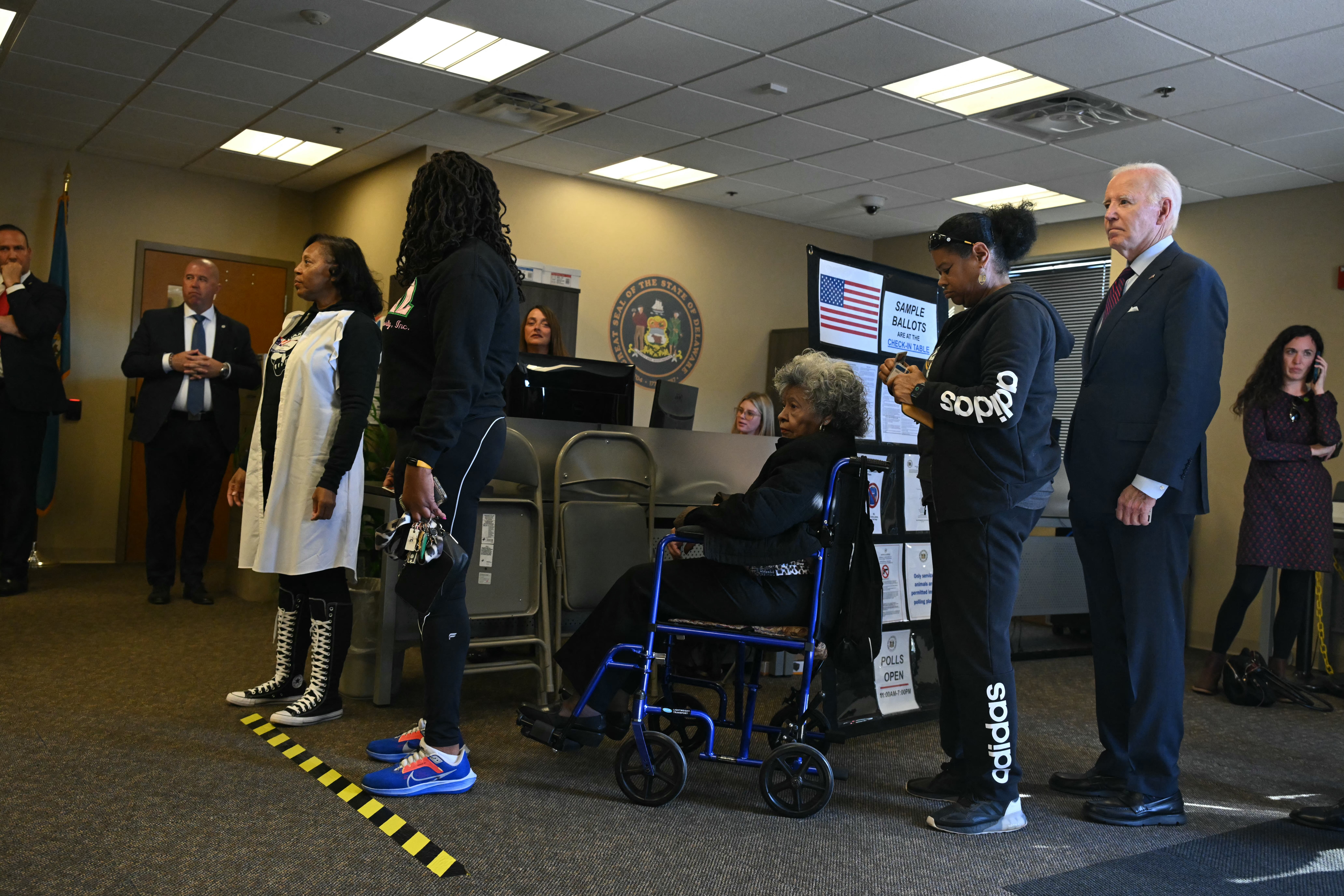 US President Joe Biden (R) waits in line with voters at a polling station in New Castle, Delaware, October 28, 2024.