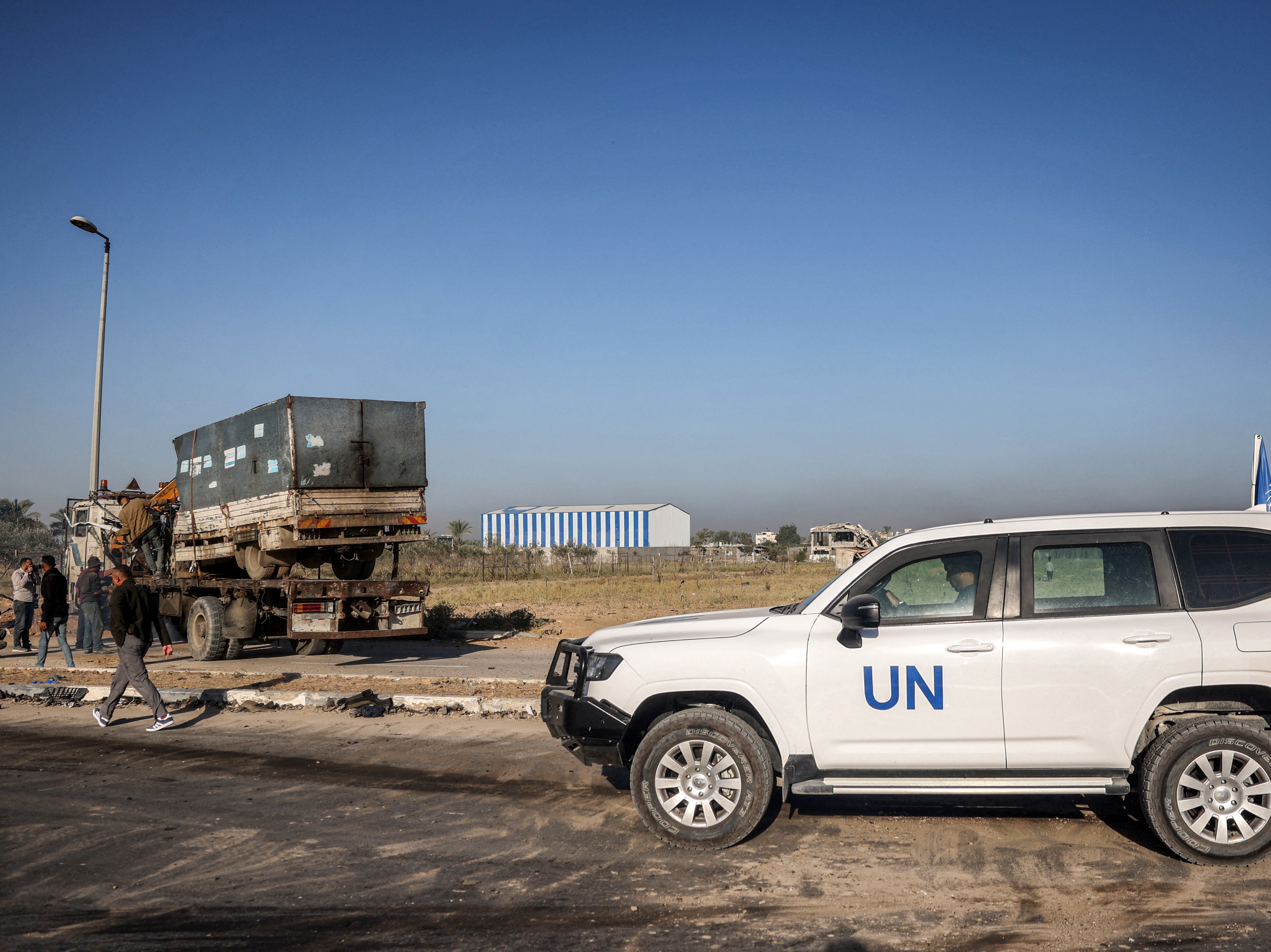 A United Nations’ vehicle is parked nearby as a destroyed truck that was reportedly used by workers of the UN Relief and Works Agency for Palestine Refugees (UNRWA), which was fired upon by Israeli forces earlier, is loaded onto the back of a trailer vehicle, along Gaza’s main Salah al-Din road outside Deir el-Balah in the centre of the Gaza Strip on 23 October 2024 amid the ongoing war in the Palestinian territory between Israel and Hamas