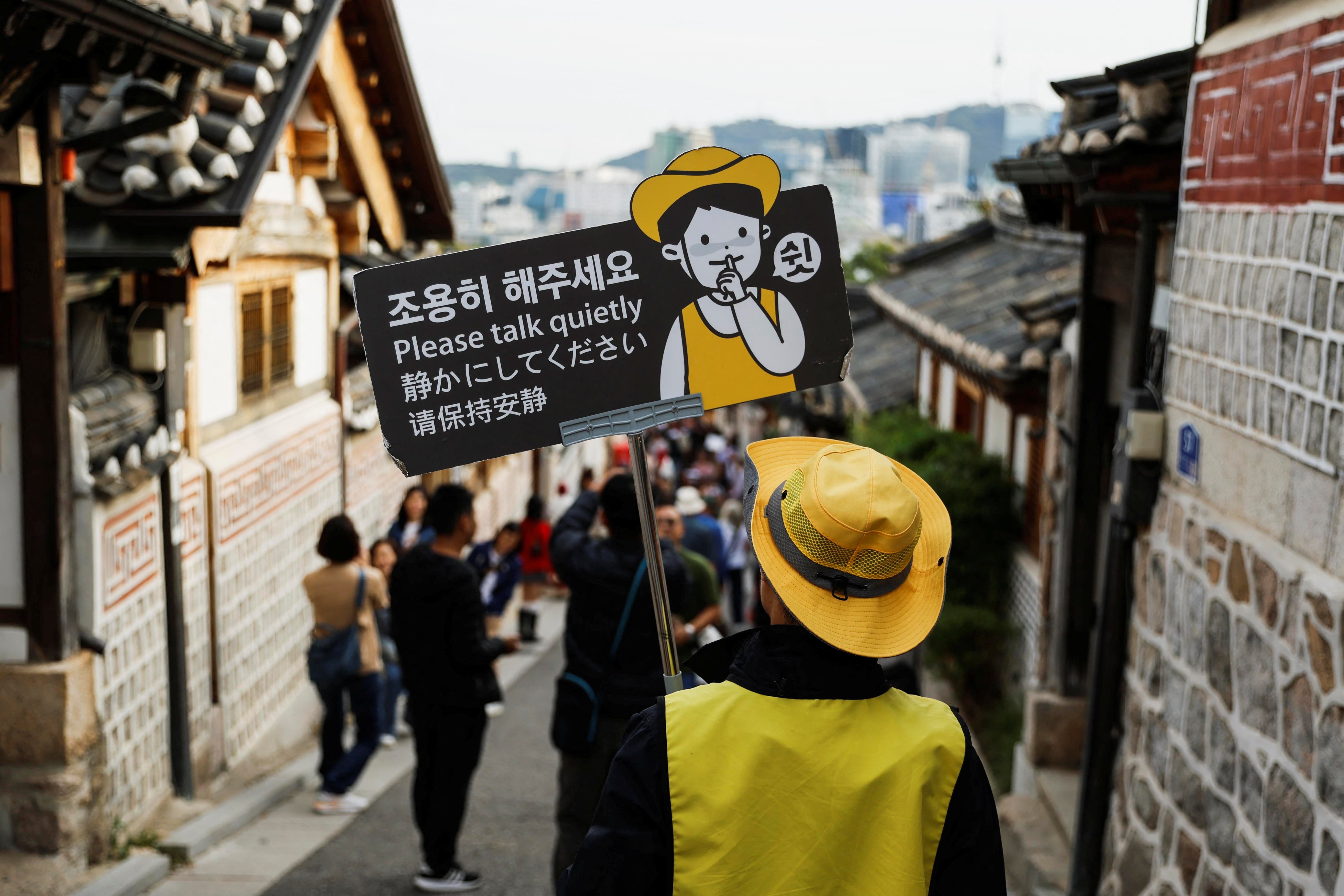 A person monitoring noise holds a sign that says 'Please talk quietly' at Bukchon Hanok Village in Seoul