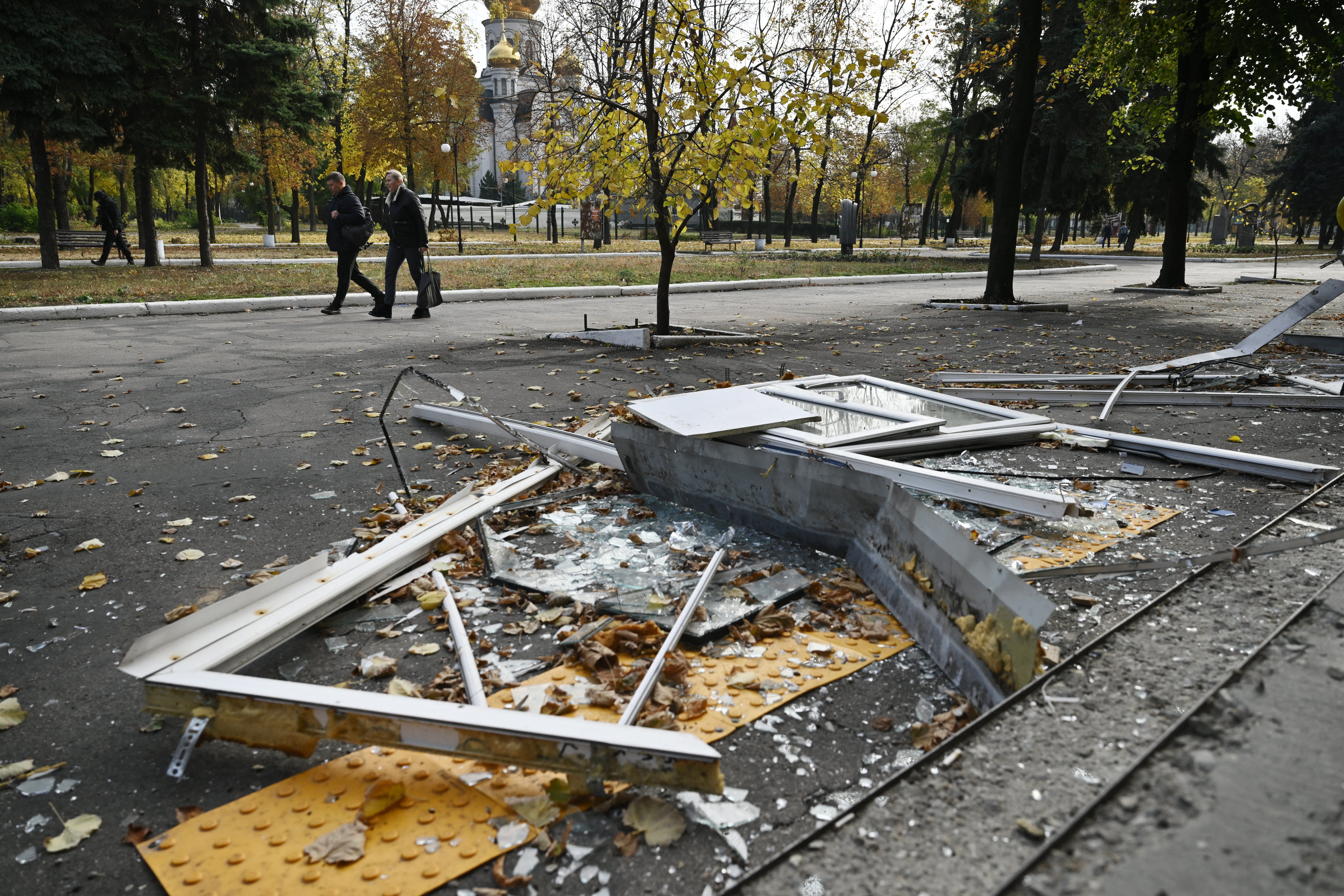 Local residents walk past broken windows on the ground near a damaged residential building, in the city of Pokrovsk, Donetsk