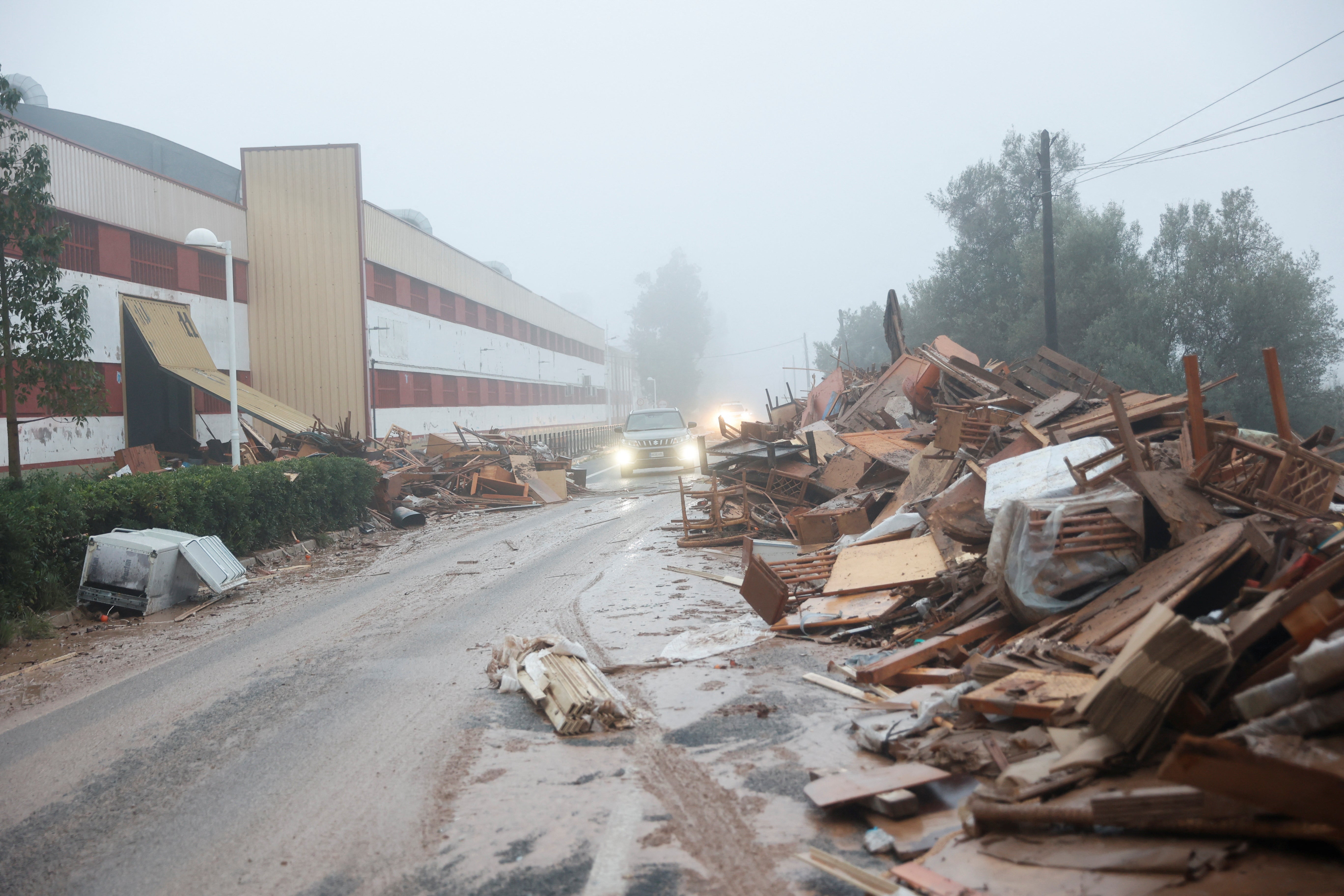 A car drives past damaged items from a furniture factory hit by the flooding in La Alcudia, Valencia