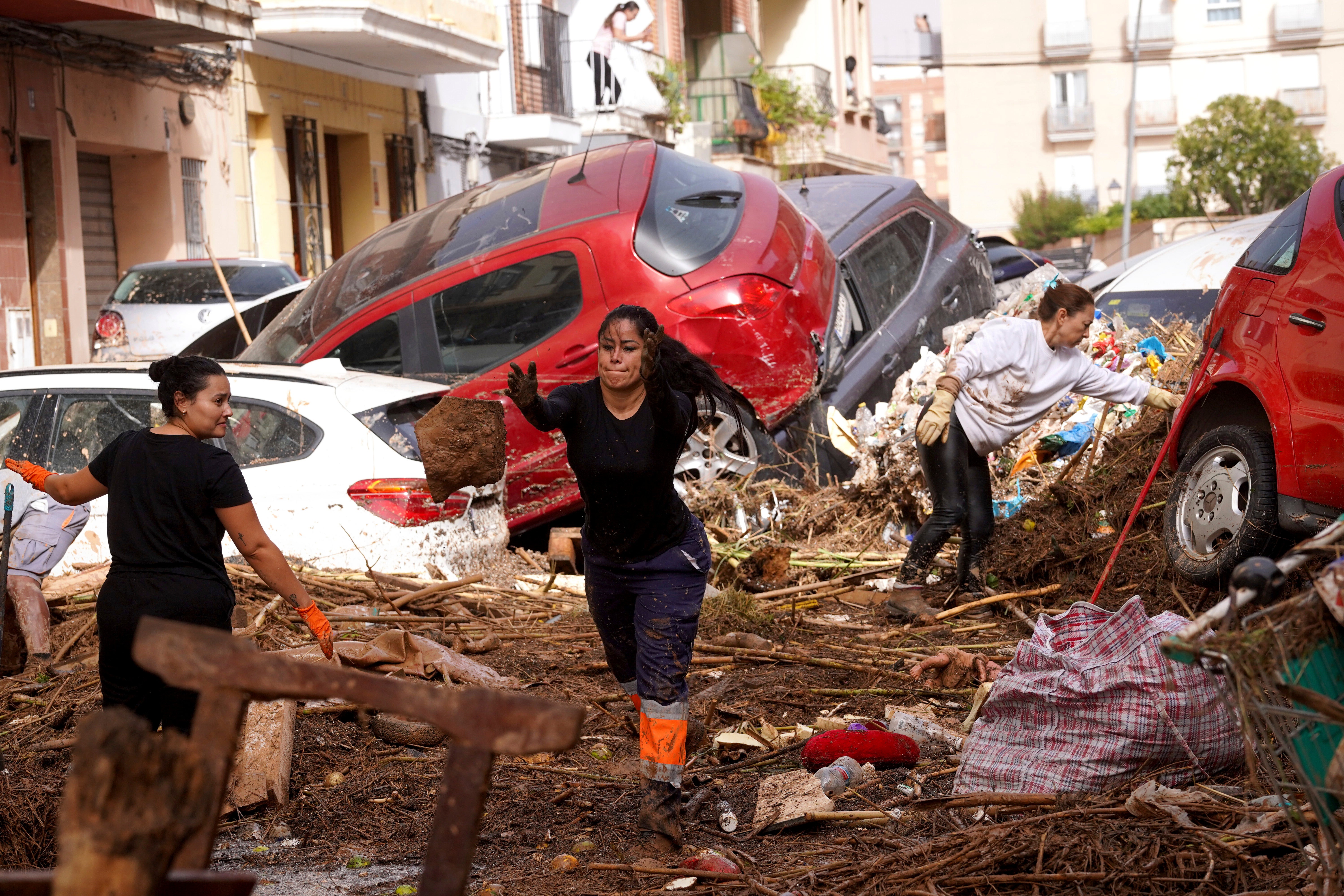 Residents clean the street next to cars piled up after flooding in Valencia