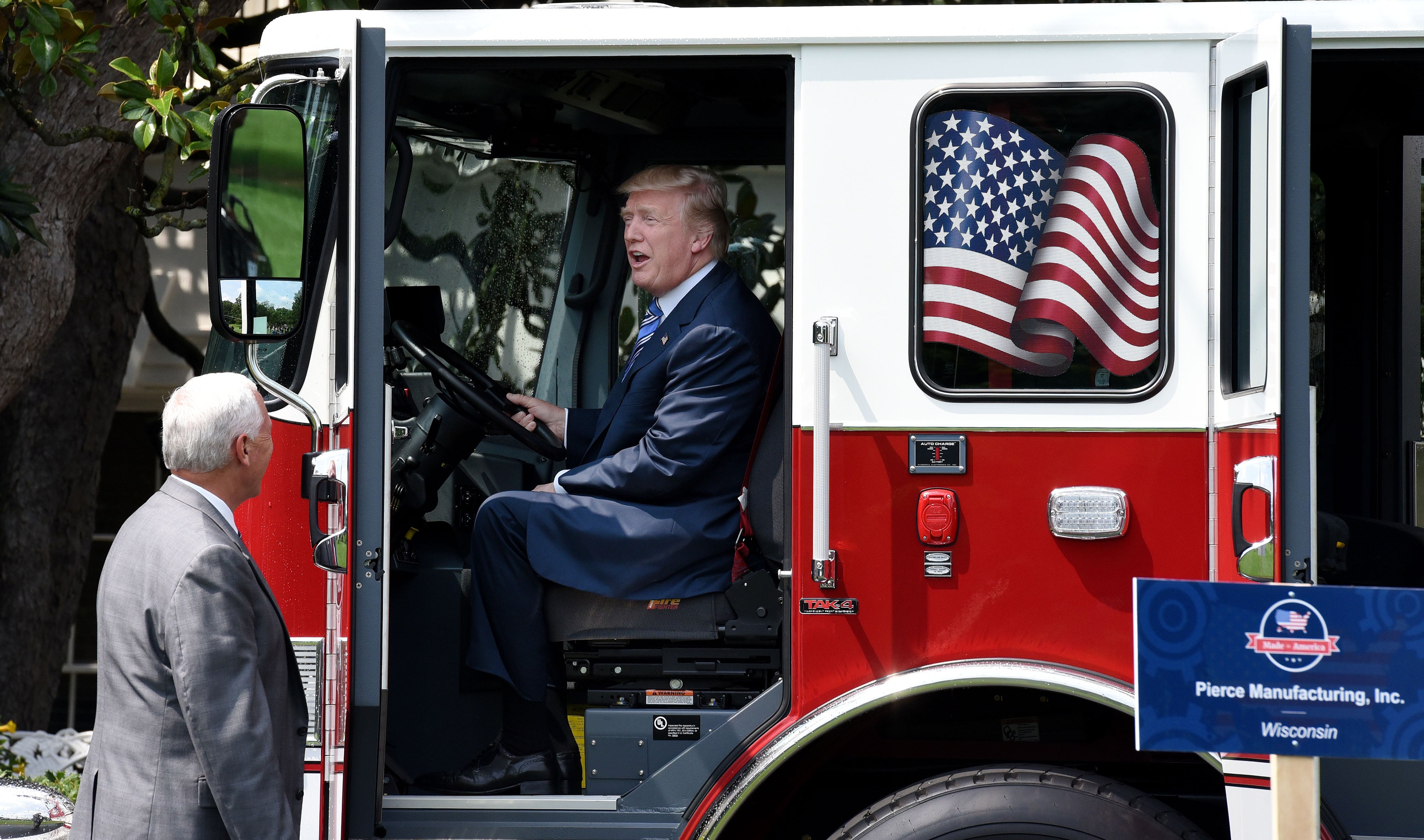 Trump smiles as he sits in a fire truck while then-Vice President Mike Pence looks on during a Made in America product showcase event on the South Lawn at the White House, on July 17 2017