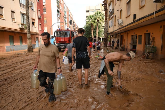 <p>People in Valancia carry water and shovel mud after flooding hit large parts of the country</p>