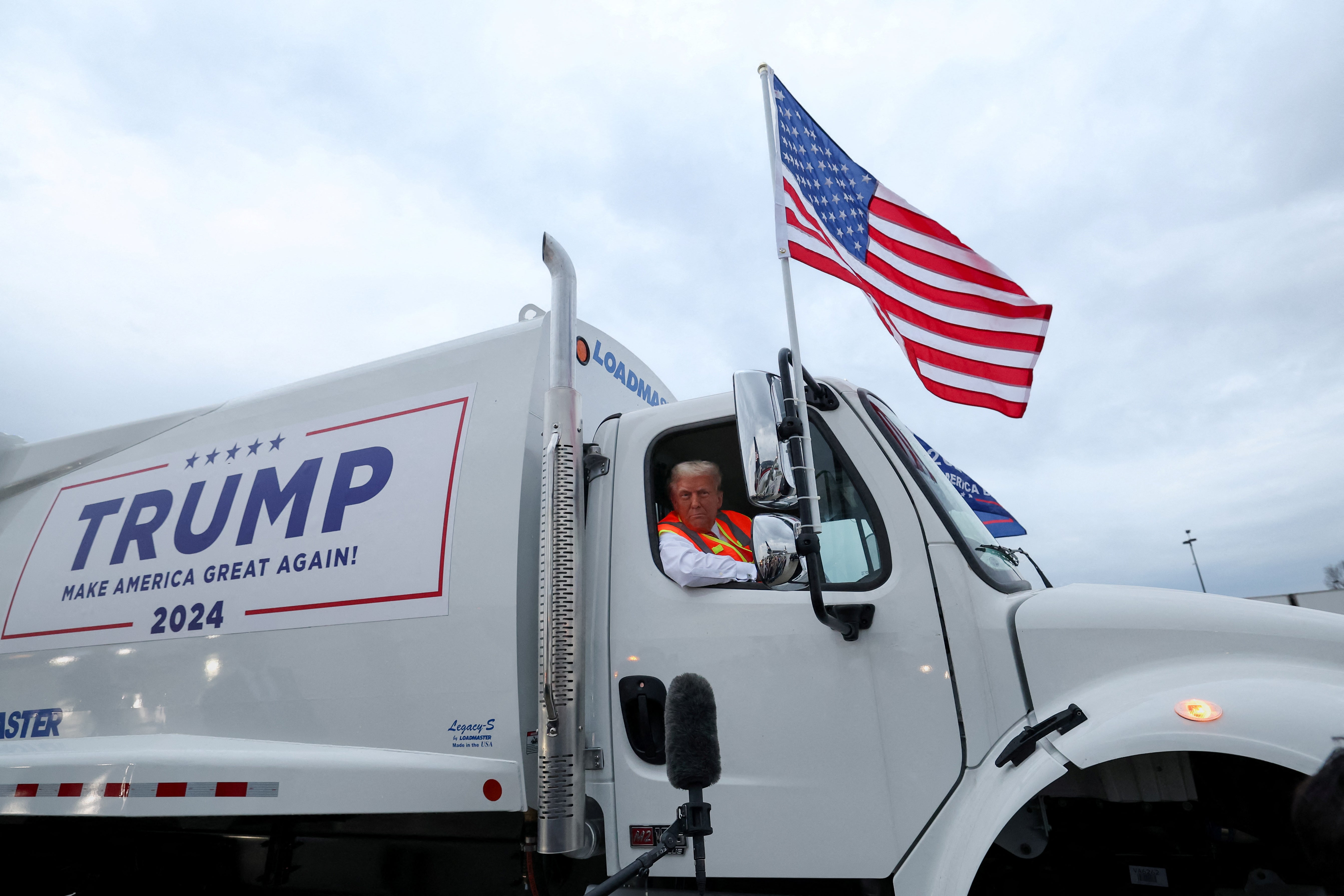 Donald Trump sentado dentro de um caminhão de lixo enquanto usa um colete de alta visibilidade, na pista do Aeroporto Internacional Green Bay Austin Straubel