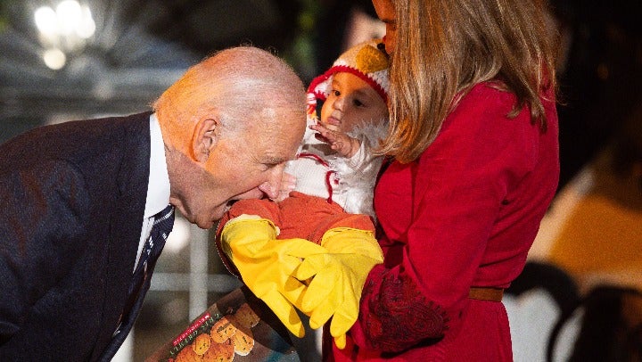 Biden playfully bites the leg of a baby dressed as a turkey at a Halloween trick-or-treating event