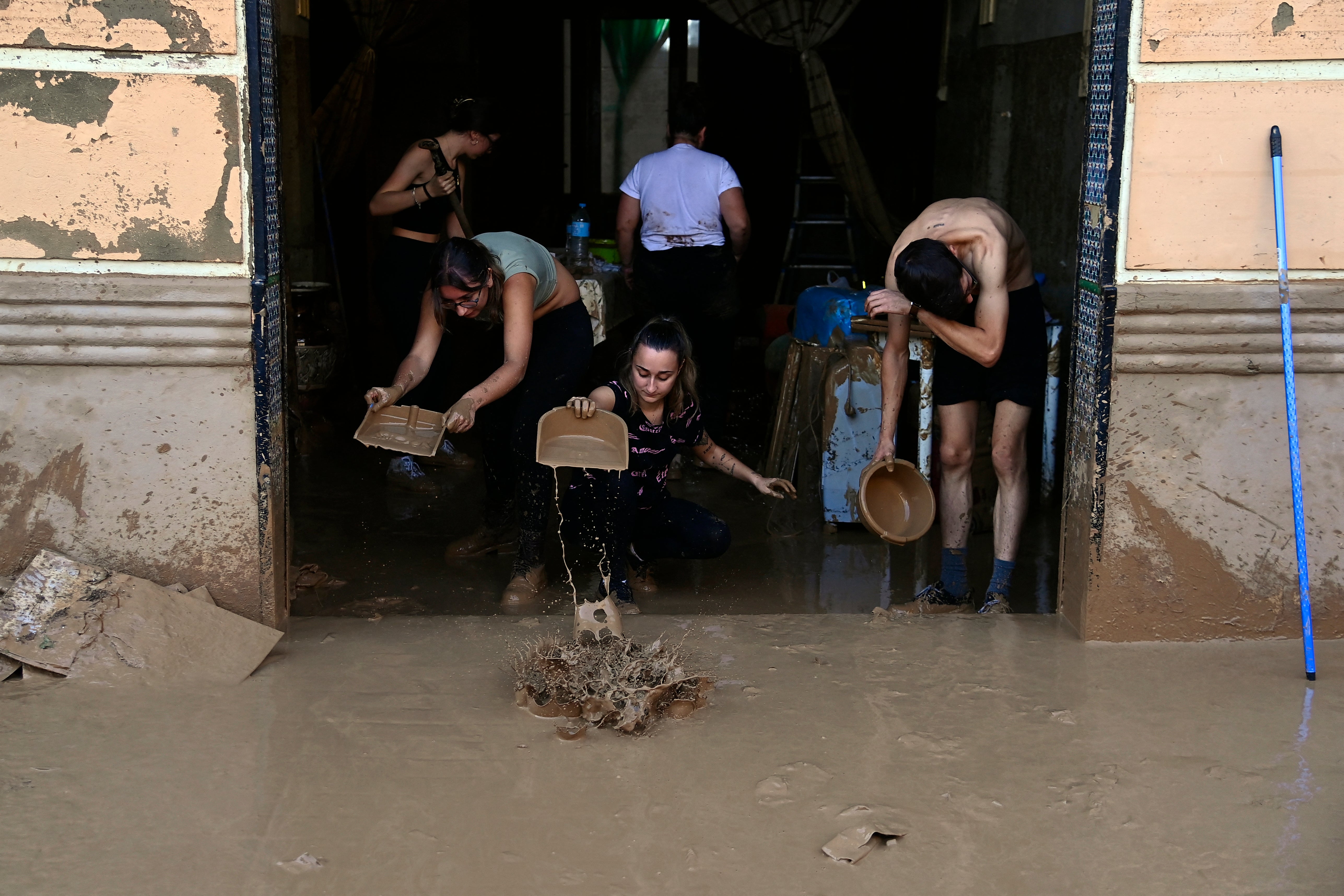 People clean a house as the street is covered in mud after flash floods affected La Torre in Valencia, Spain